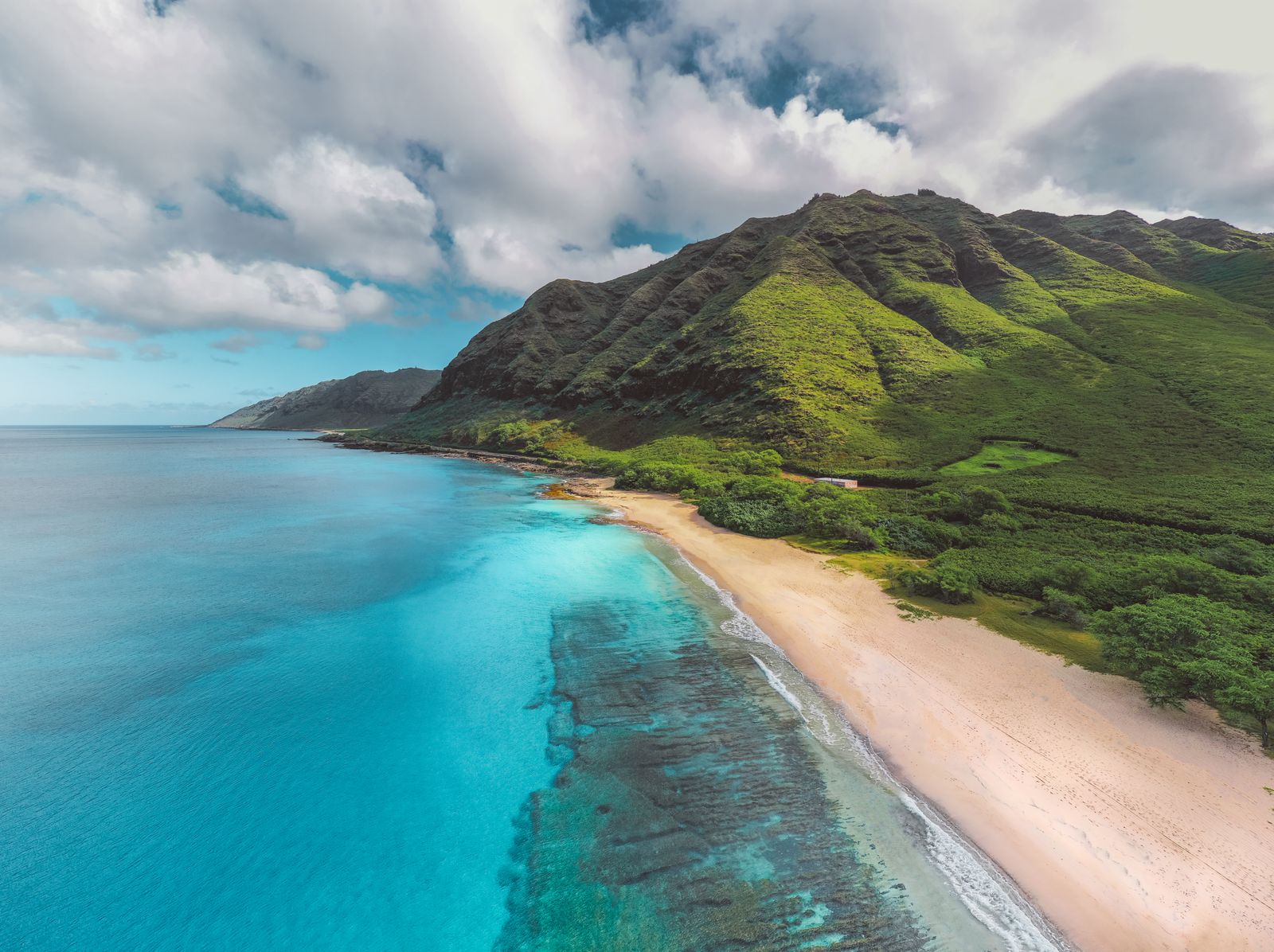 Aerial view of a green tropical coastline meeting turquoise ocean water, the kind of Hawaii packing list scenery worth planning for