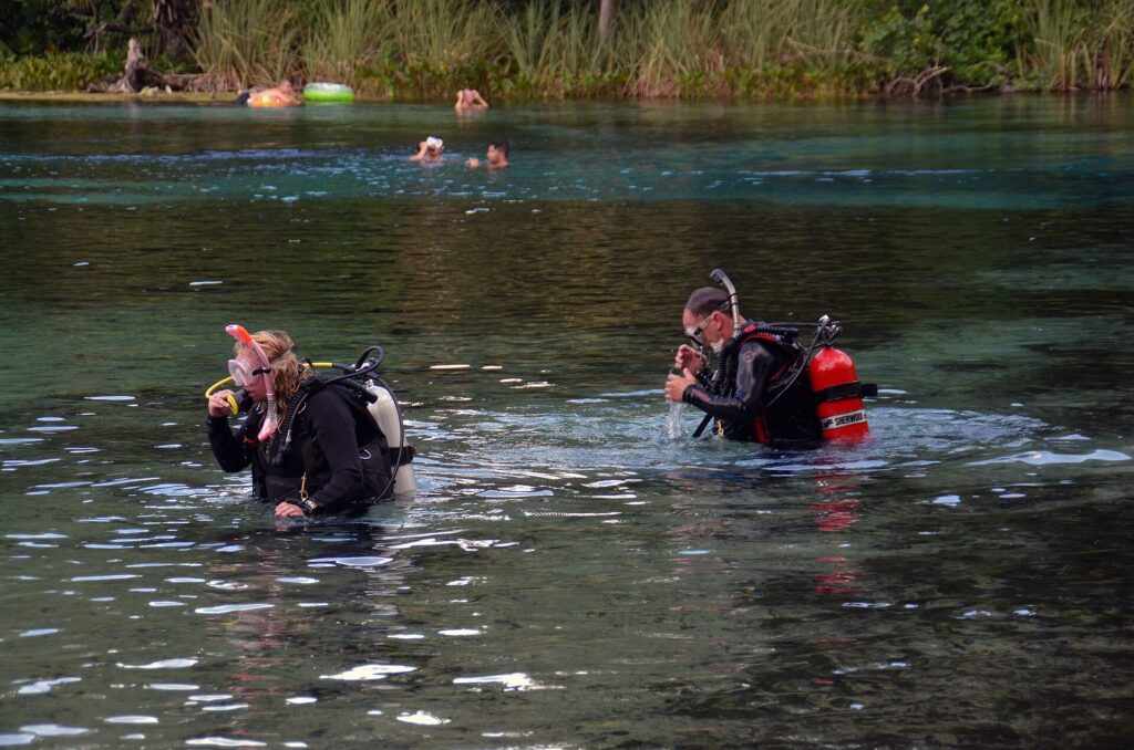 Two divers in scuba gear wading into the water at Alexander Springs while swimmers float in the background