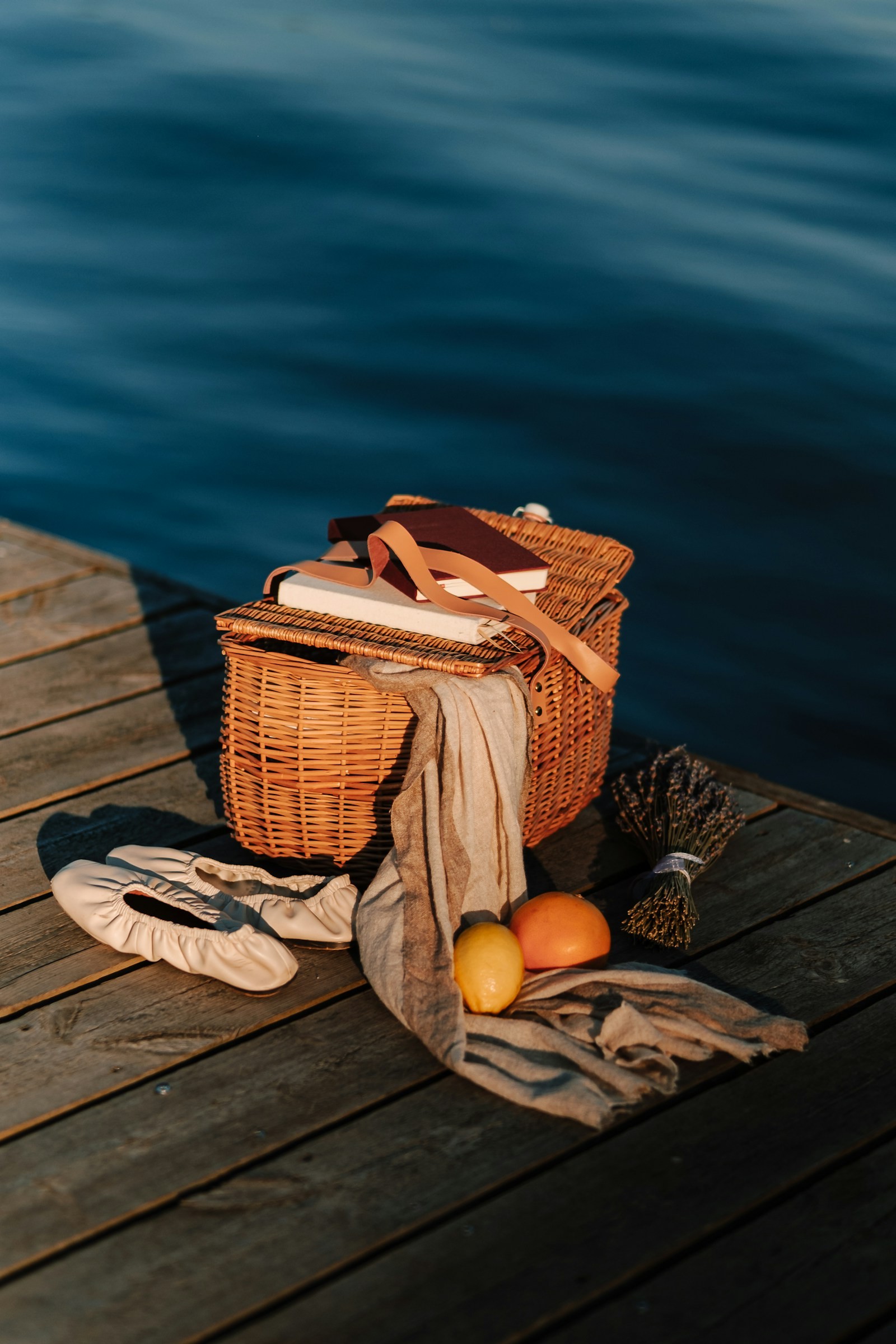 A basket and fresh fruit on a dock beside the water.
