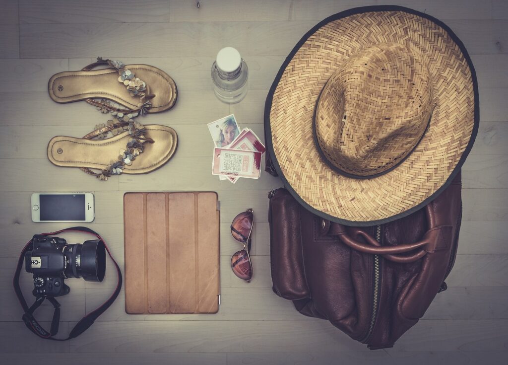 Sandals, a camera, sunglasses and a sun hat laid out with other travel items