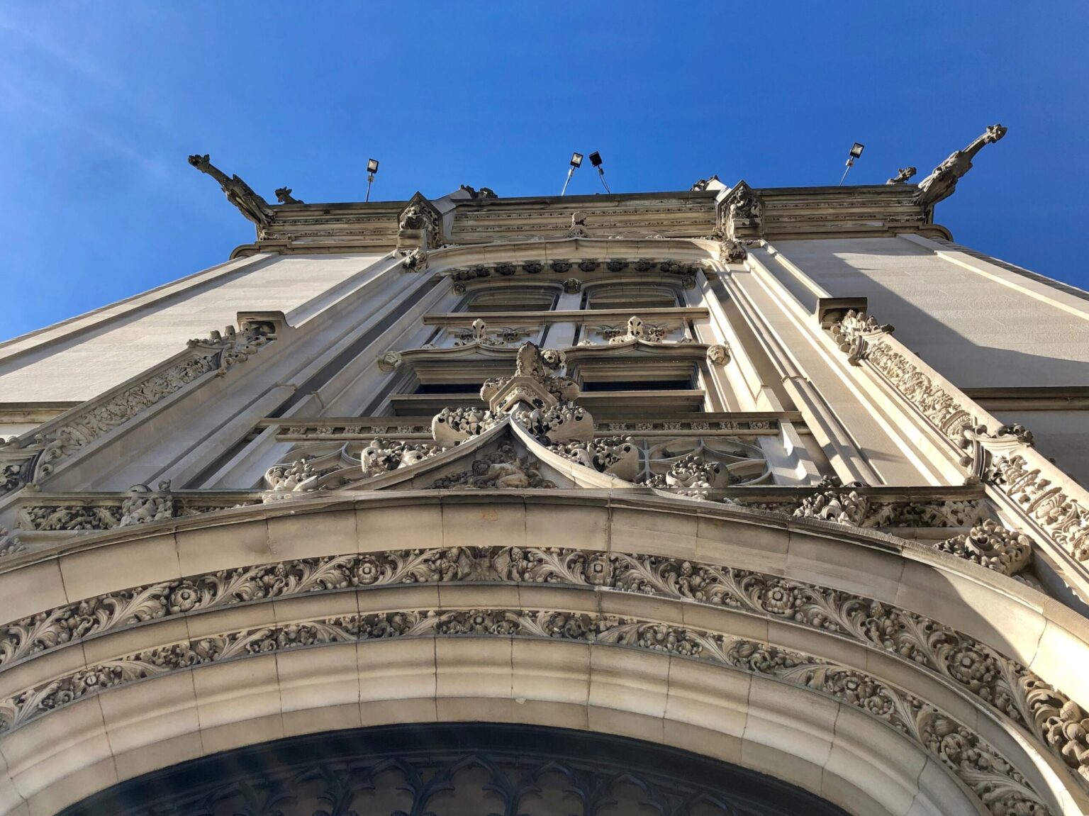 Carved limestone tracery and gargoyles above an arched entrance of Biltmore House, looking up against a blue sky