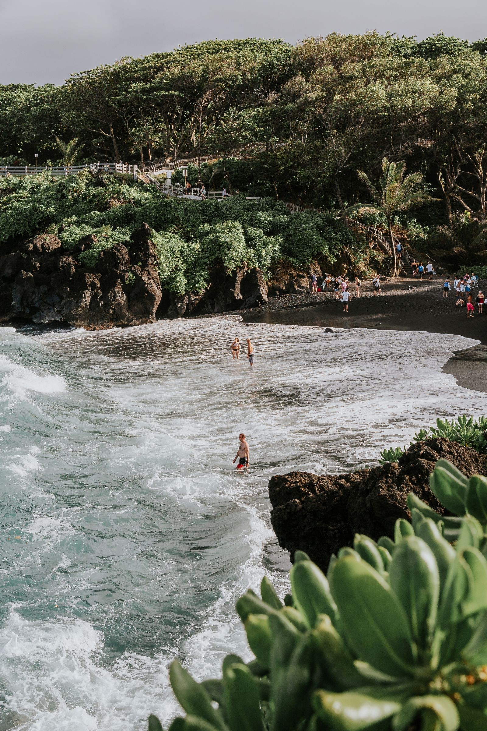 A black sand beach along Maui's Hana coast with waves and cliffside greenery