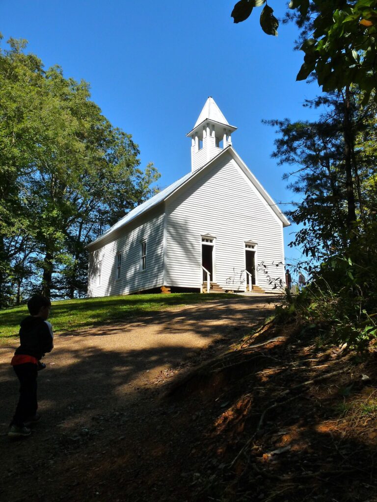 Historic white wooden church at the base of a wooded hillside in Cades Cove