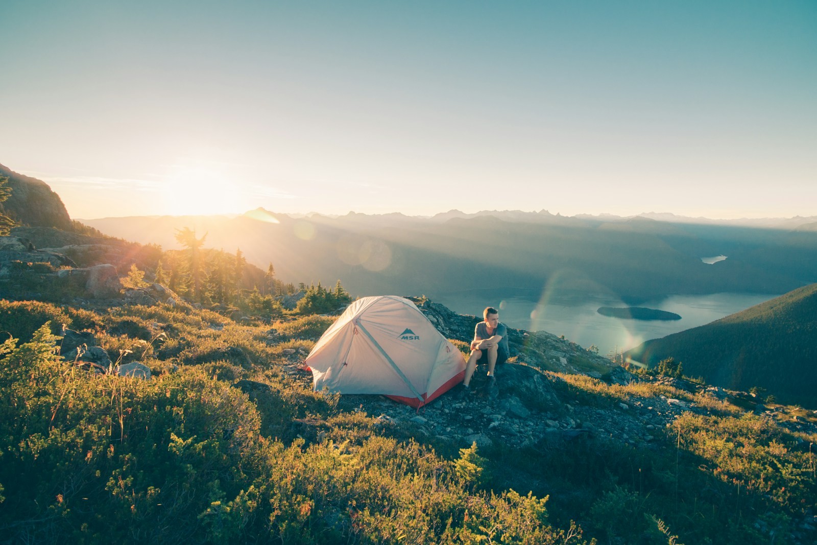 A camper sitting on a rock beside a white tent.