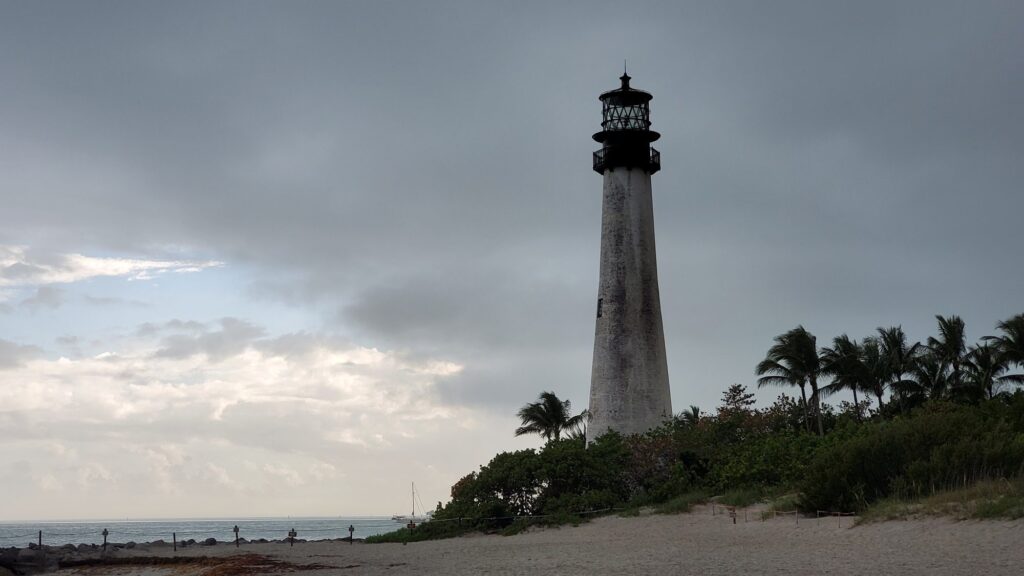 Cape Florida Lighthouse under grey clouds with palms and beach, Key Biscayne