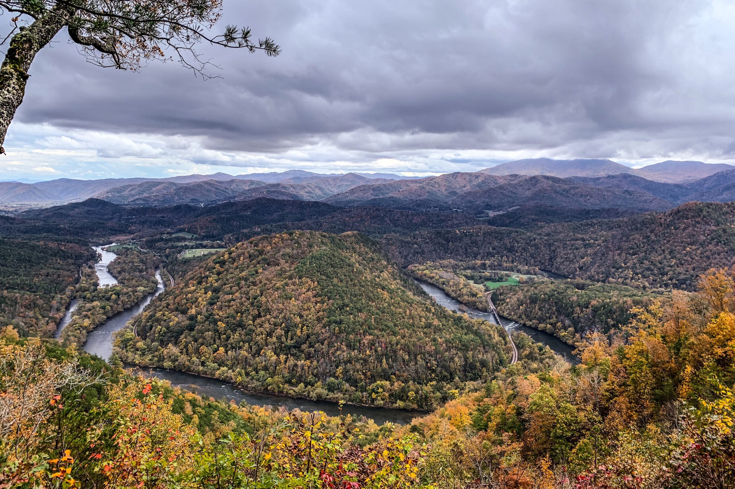 The French Broad River bending through forested ridges in fall color, seen from the Chimney Rocks overlook in Cherokee National Forest under a grey sky