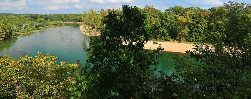 Wide view of the Current River bending through wooded Ozark hills with a gravel bar