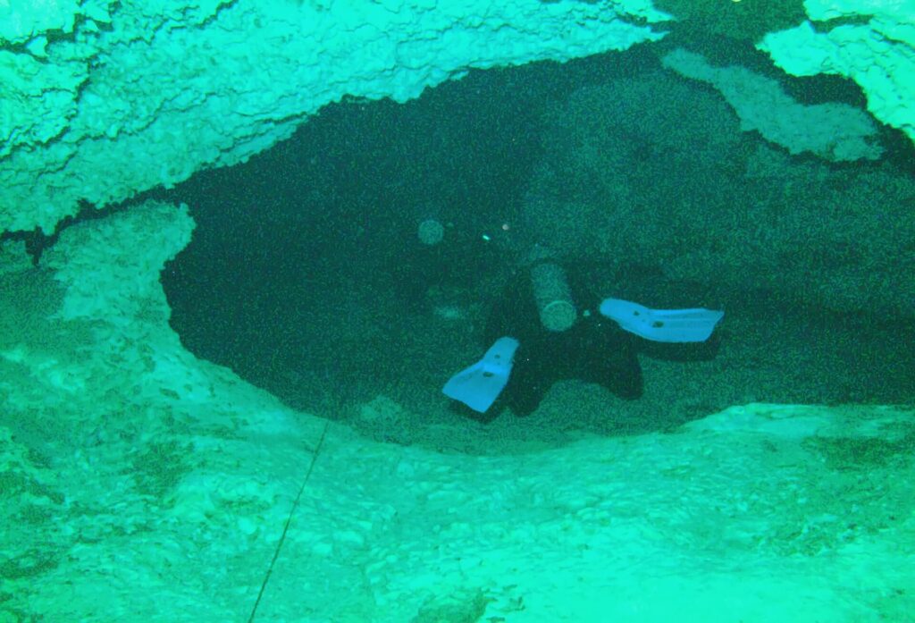 A snorkeler swims past a rock formation in the clear water of Dos Ojos Cenote near Tulum