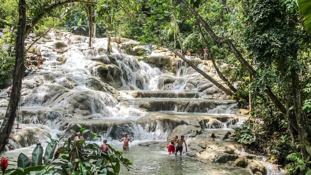 Visitors wading at the base of Dunn's River Falls with the terraced cascades rising behind them