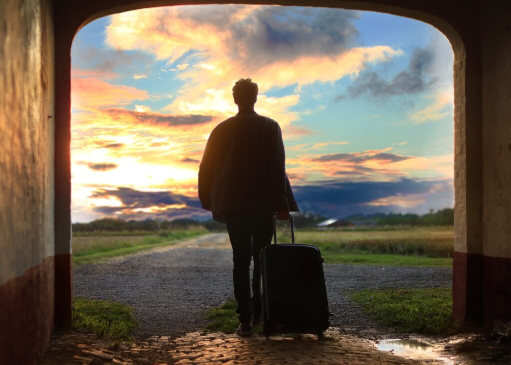A traveler silhouetted while pulling a rolling suitcase through an archway at sunset