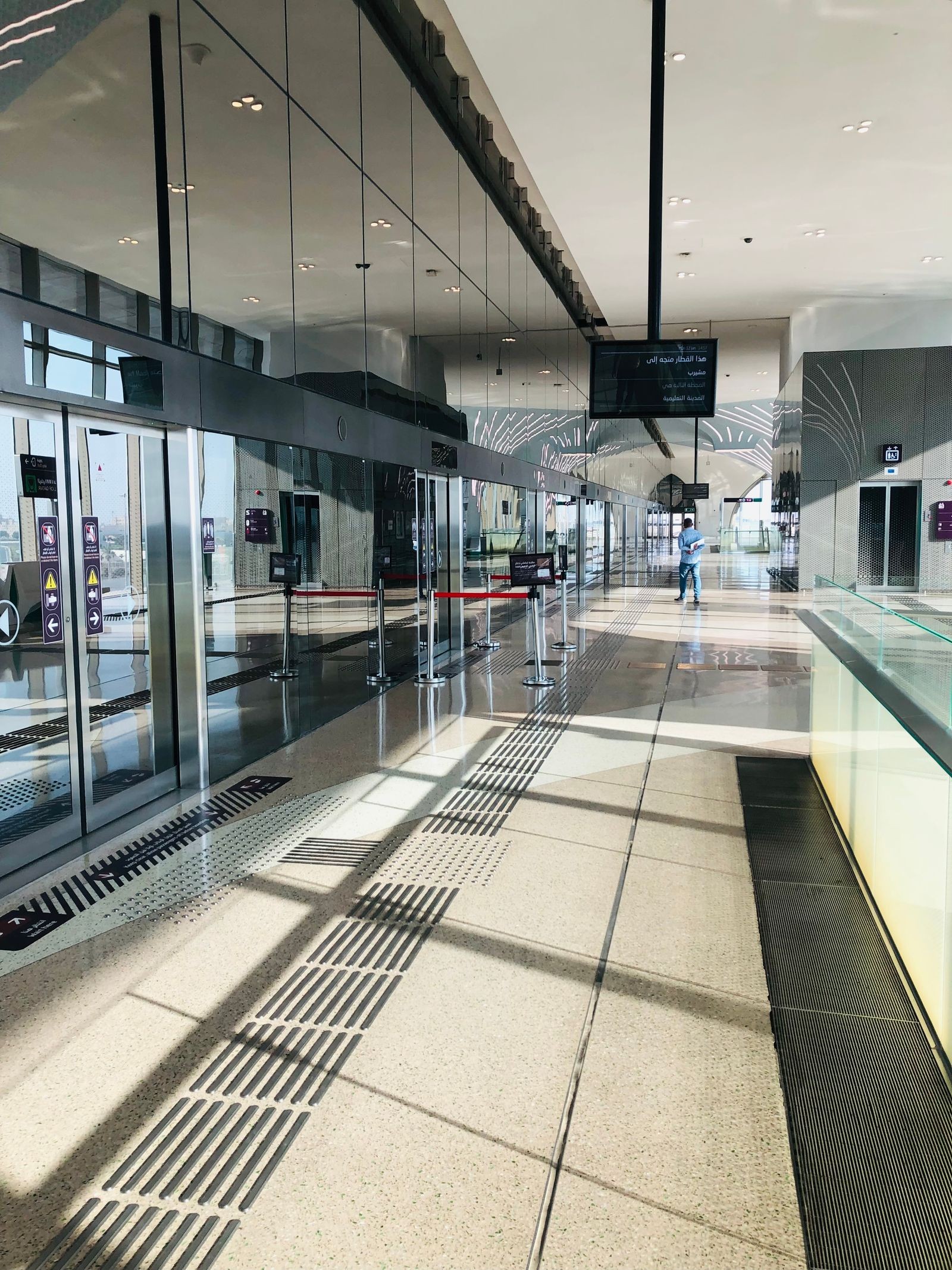 A long, nearly empty airport terminal hallway with glass walls and overhead signage