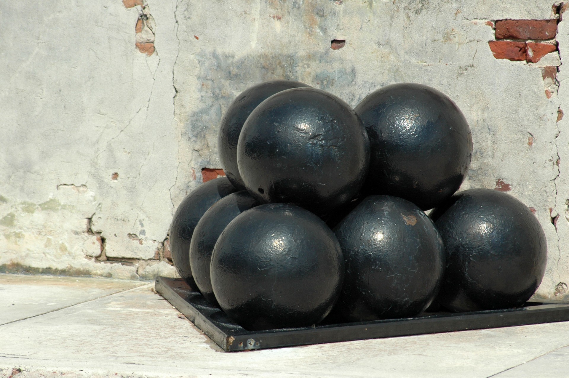 A pyramid of black iron cannon balls on a metal tray against an old plaster and brick wall at Fort Zachary Taylor