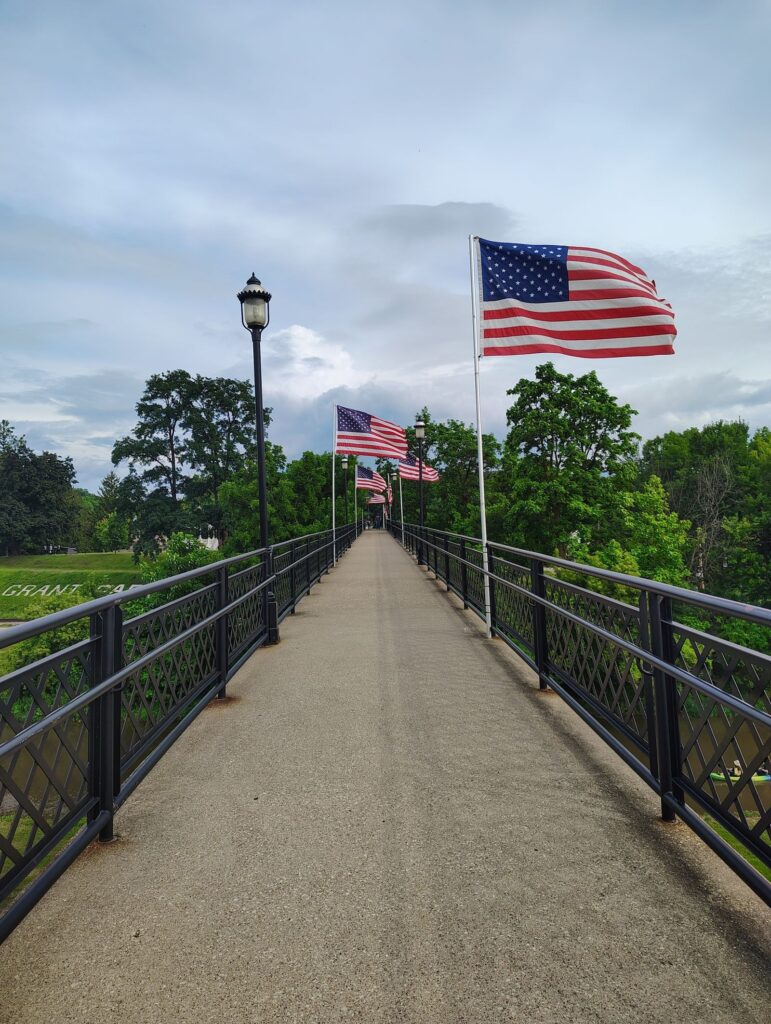 A pedestrian bridge lined with American flags leading toward Grant Park in Galena, Illinois