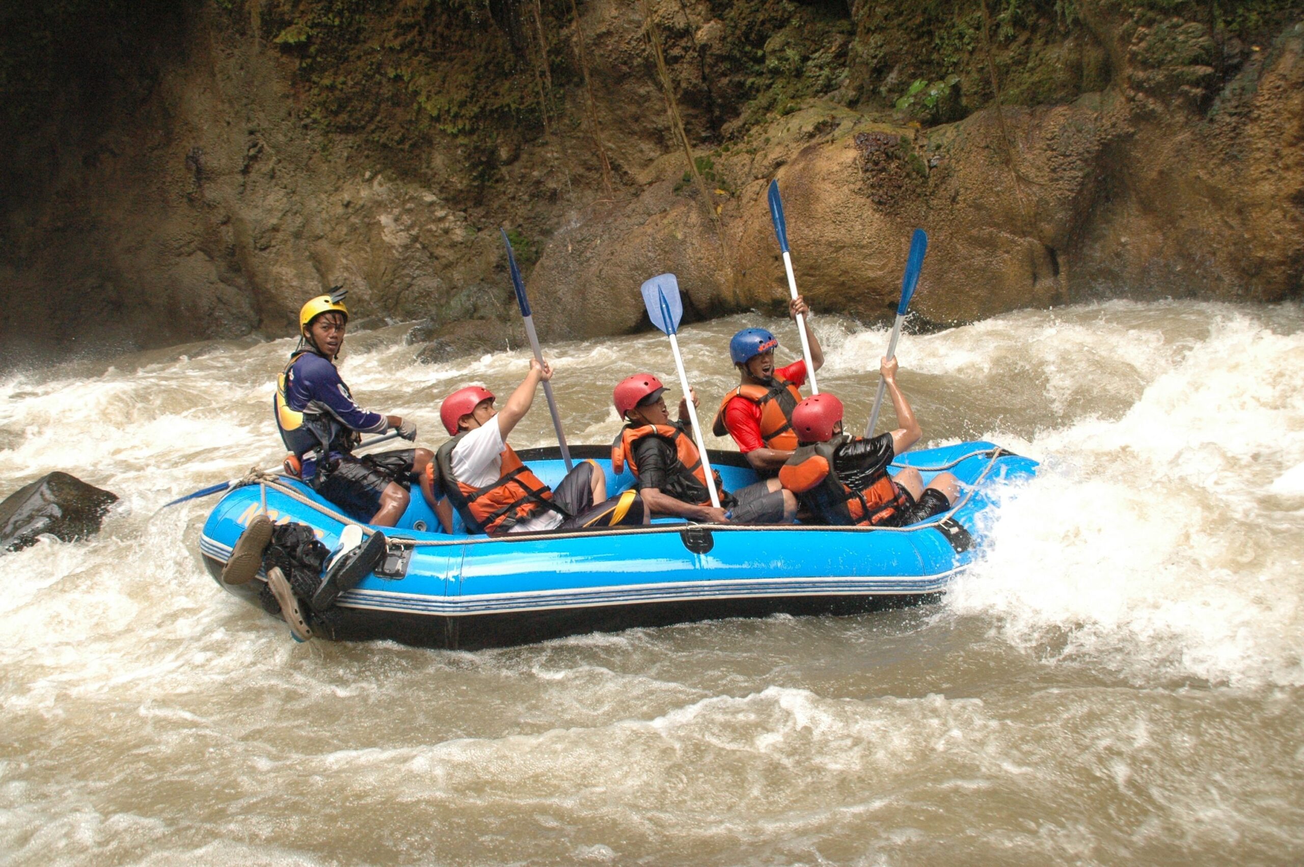 A group of rafters paddle an inflatable raft through churning whitewater rapids