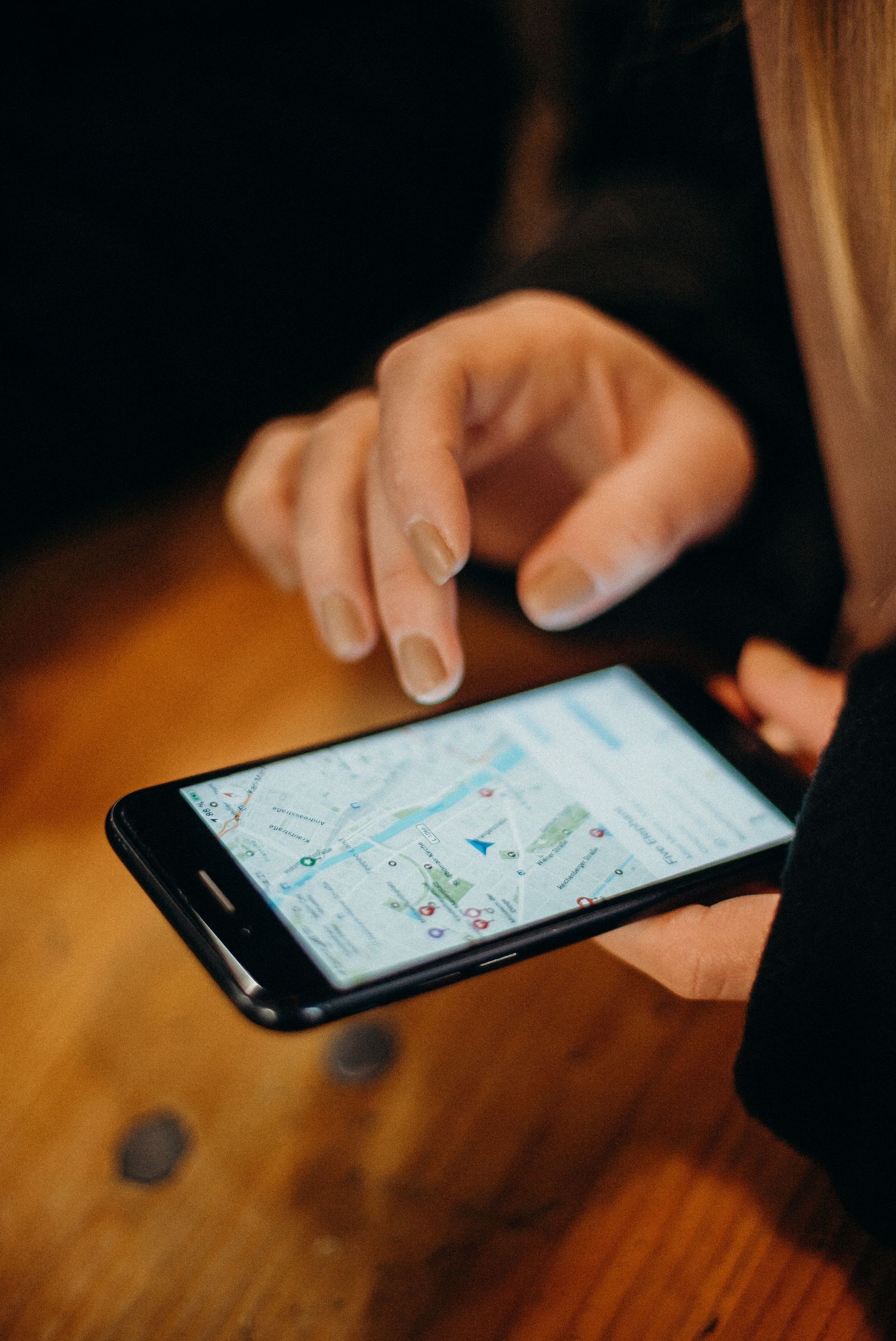 Two hands pinch-zooming a map on a smartphone screen resting on a wooden table