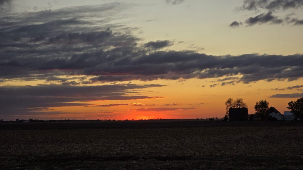 Sunset over a harvested Illinois cornfield with a red barn and farmhouse silhouetted