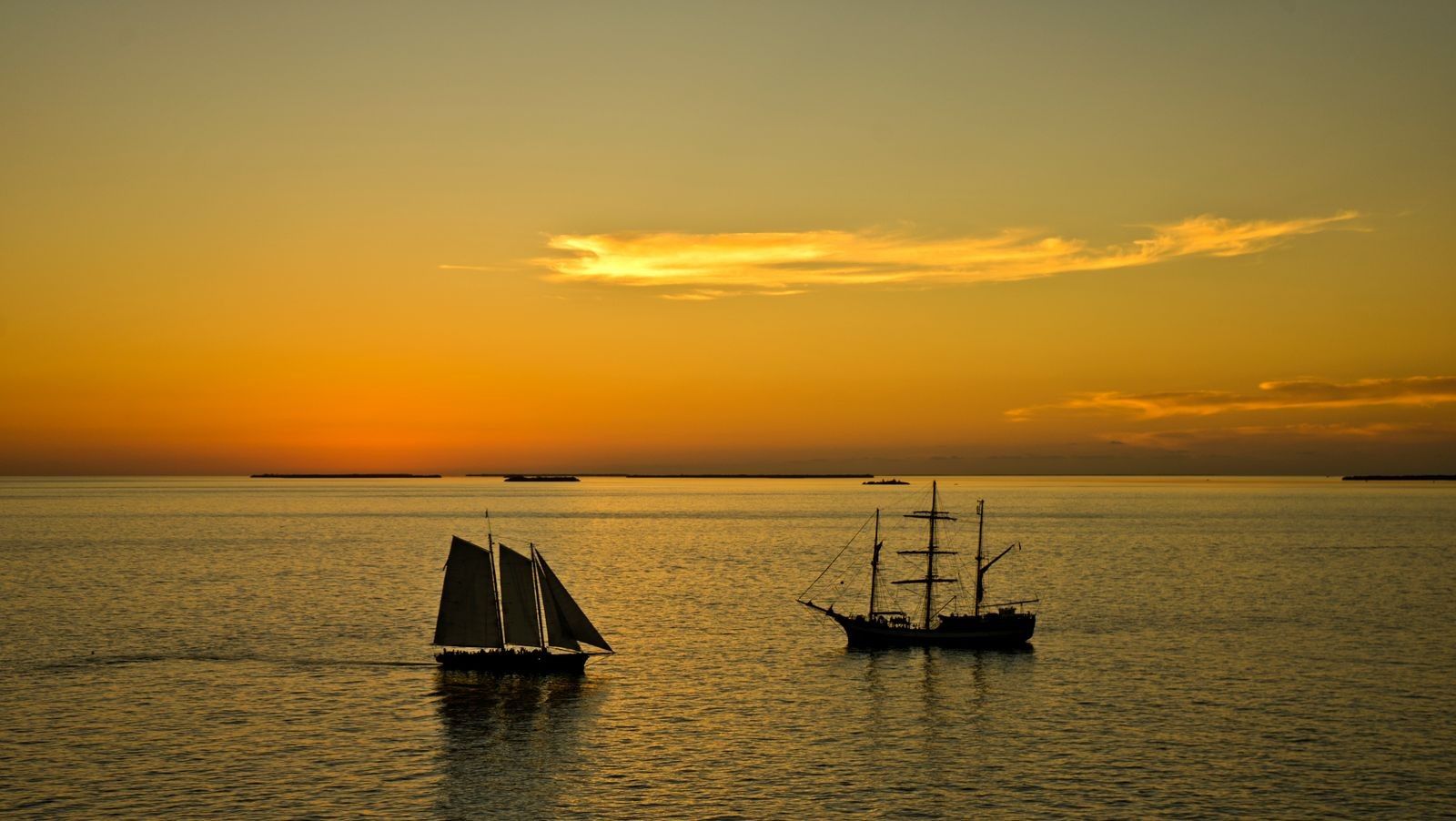 Two tall sailing ships silhouetted on calm water off Key West under an orange sunset sky
