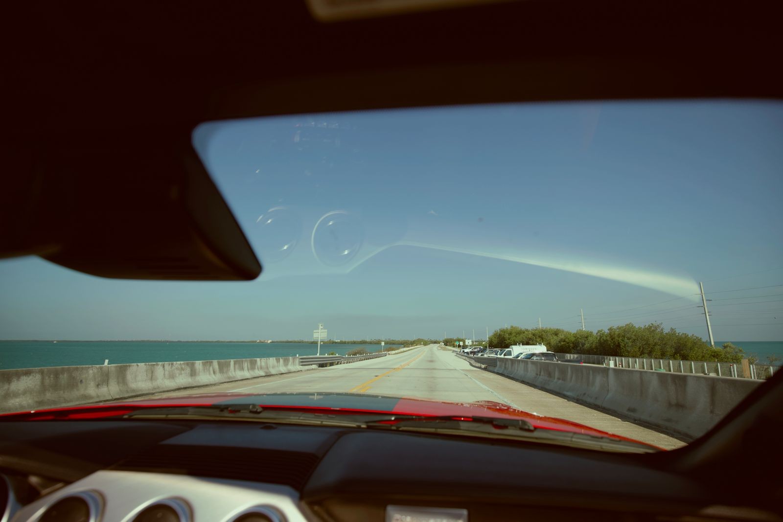 Driver view through the windshield crossing an Overseas Highway bridge in the Florida Keys, concrete barrier and turquoise water on both sides