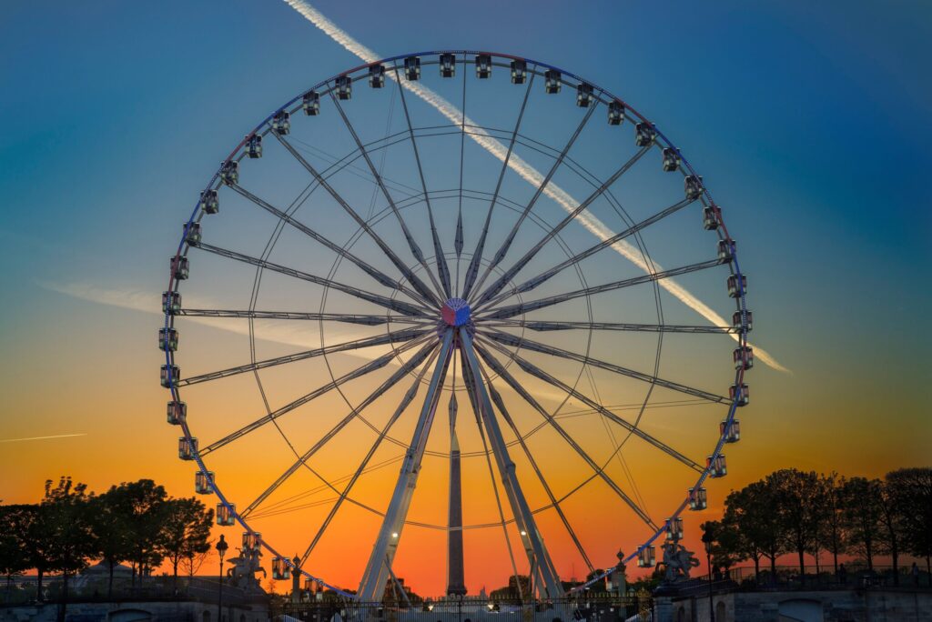 A large Ferris wheel silhouetted against a vibrant sunset at an amusement park