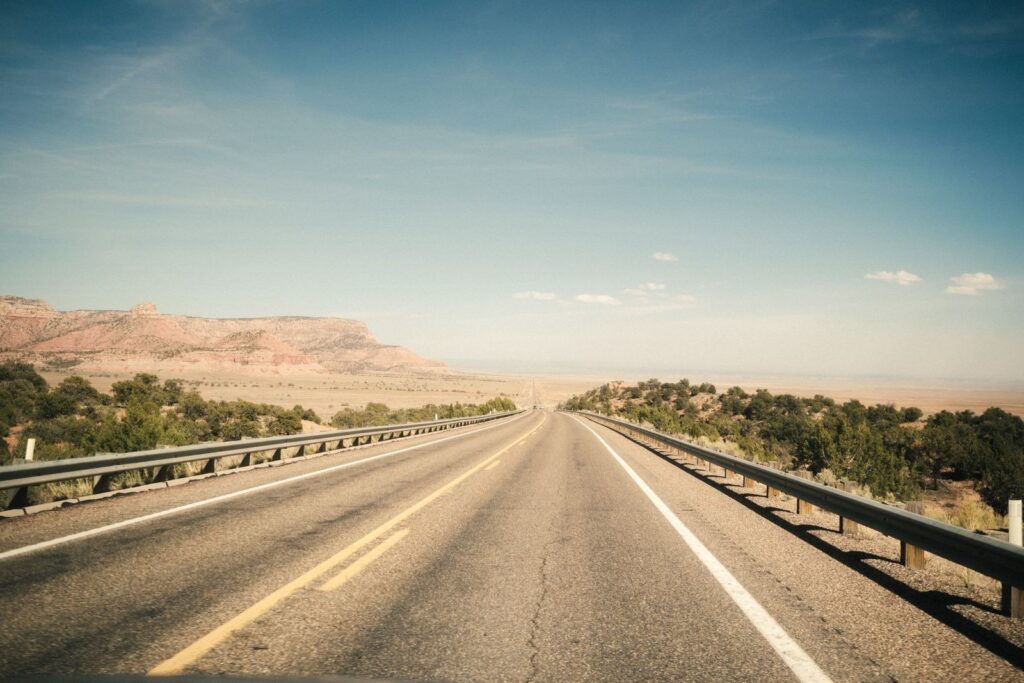 Empty two-lane desert highway stretching toward distant red-rock mesas under a clear sky