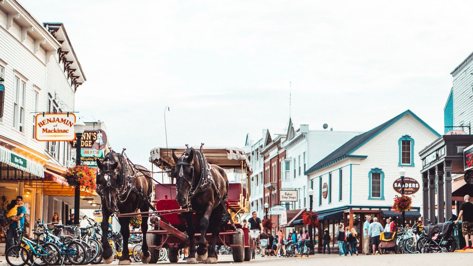 Mackinac Island Main Street with a two-horse dray, racks of rental bikes along the curb and storefronts behind