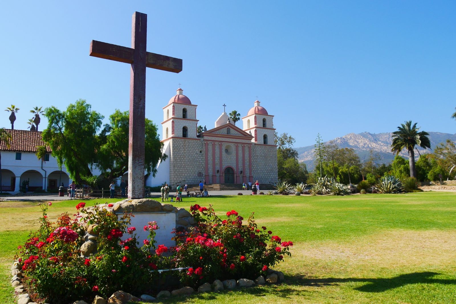 A large cross and rose bushes in front of Old Mission Santa Barbara