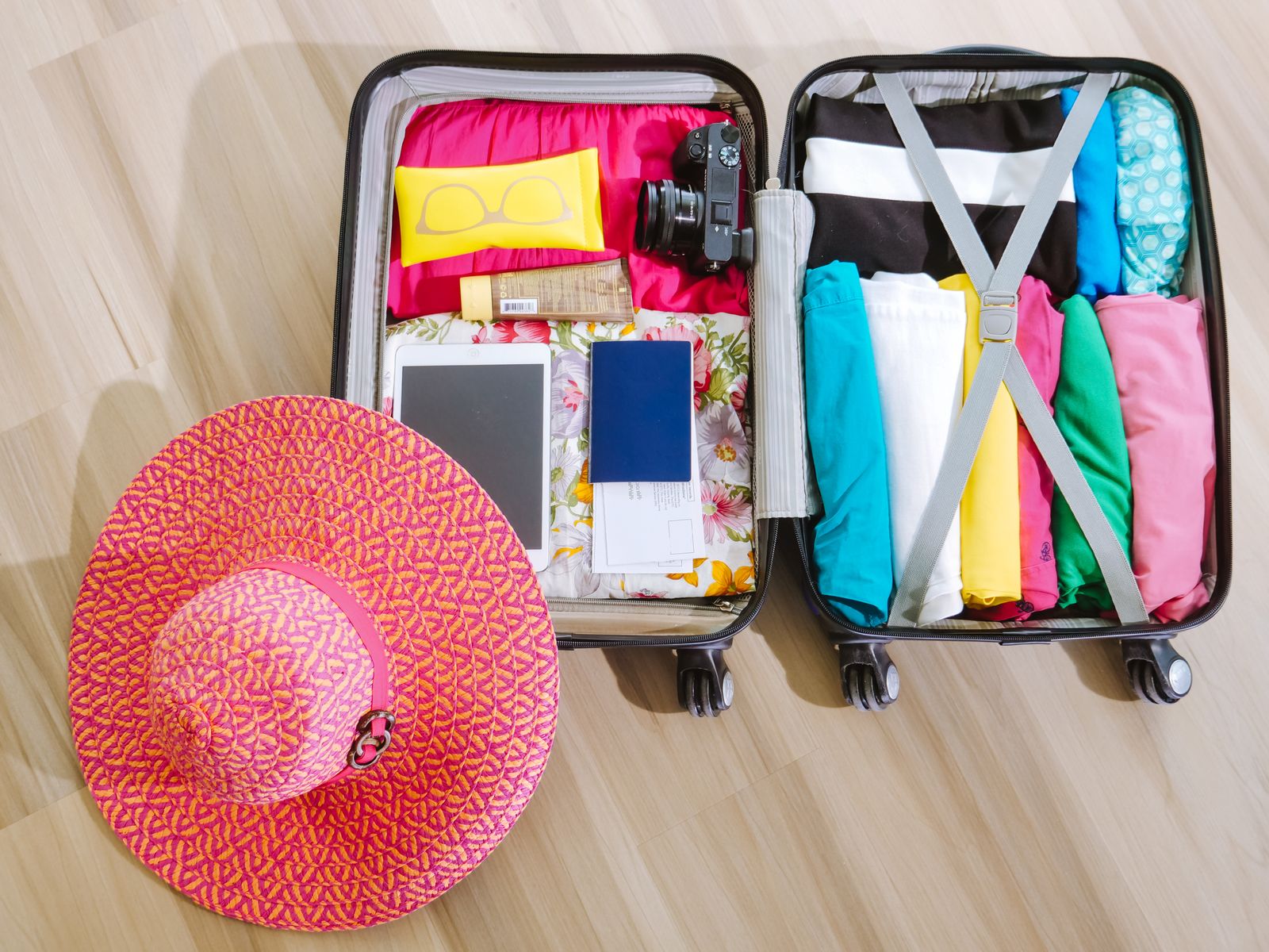 An open suitcase packed with folded clothes, a camera and travel accessories