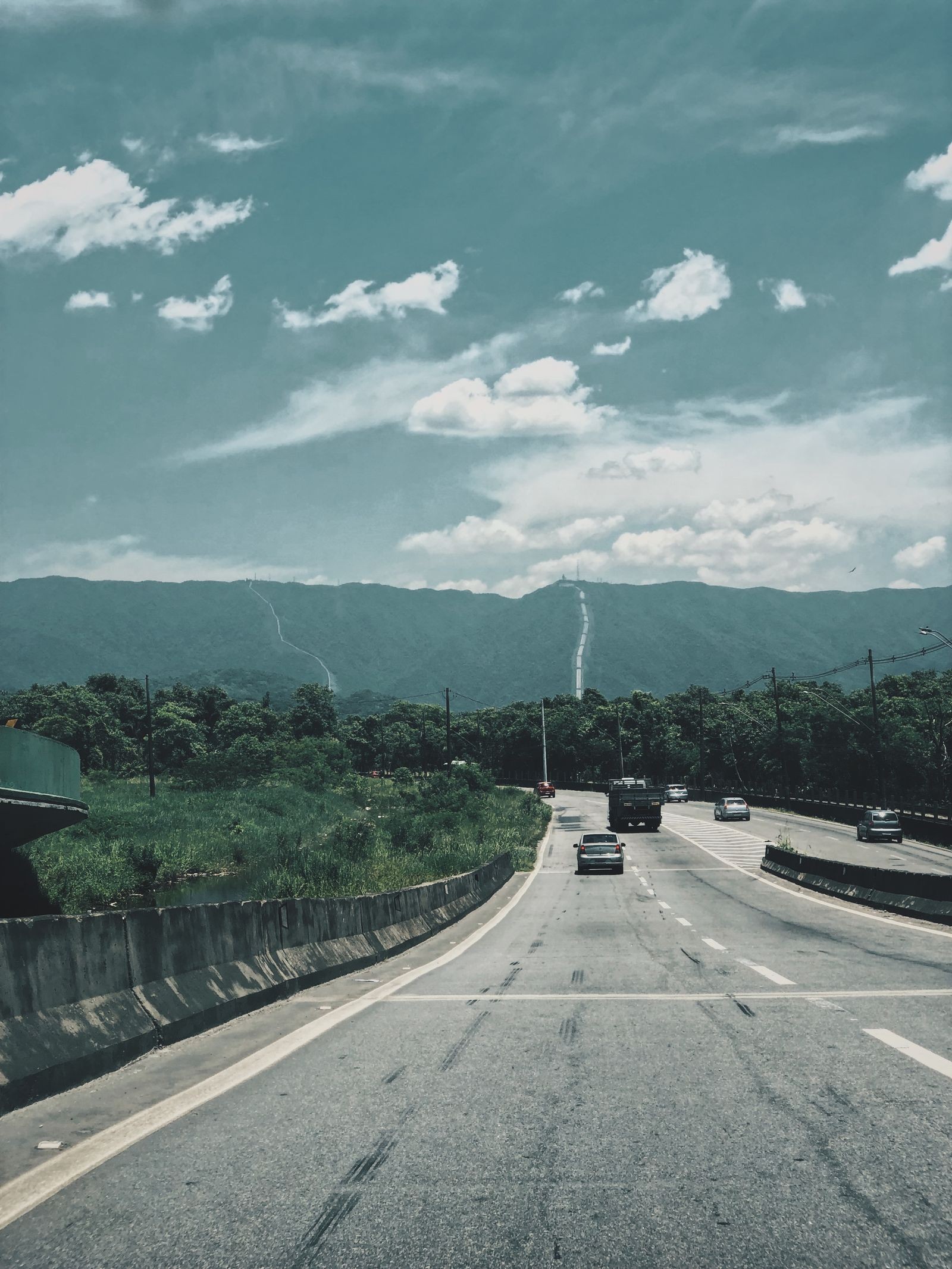 A highway curving through wooded hills under a partly cloudy sky