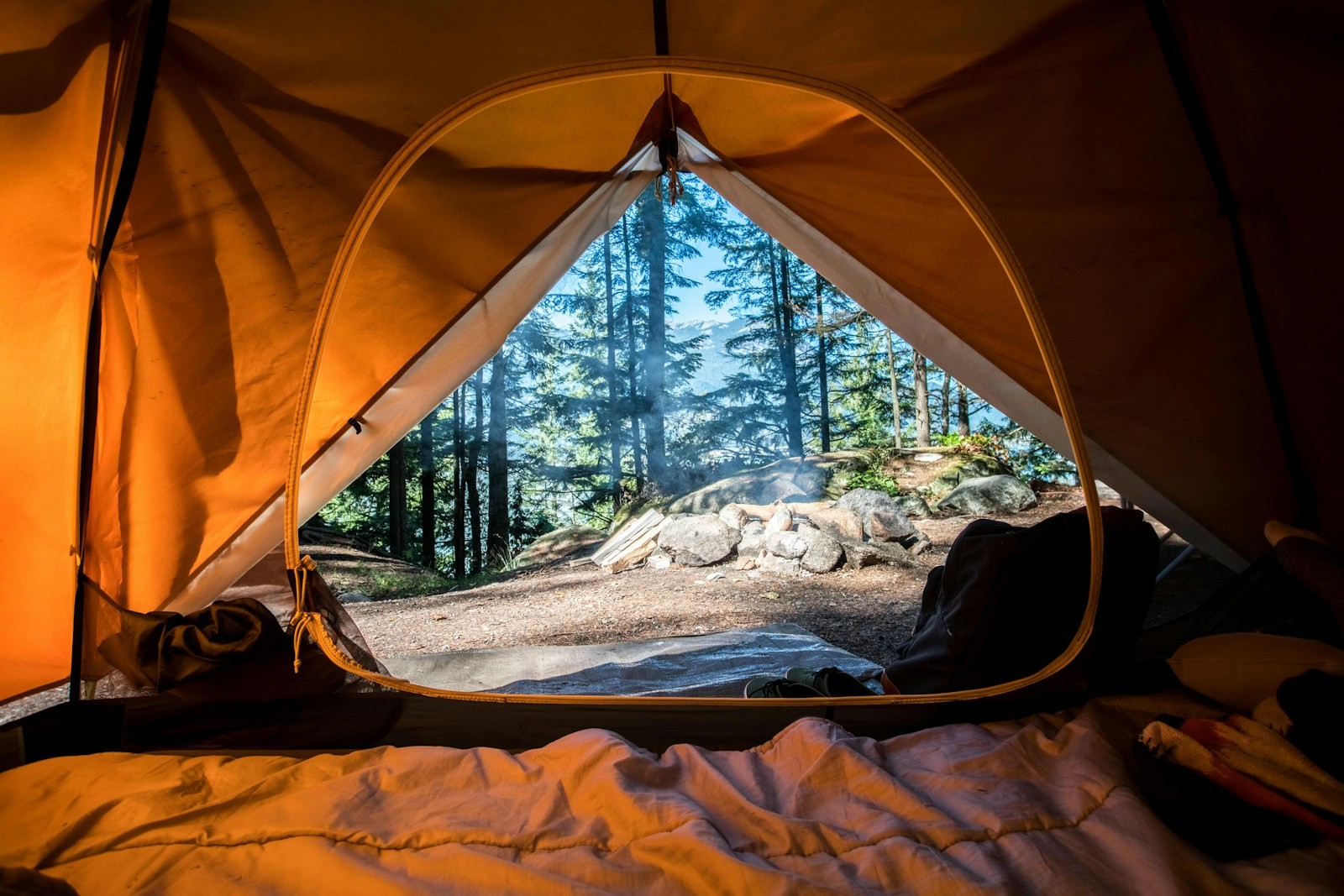 An orange tent pitched near green trees.
