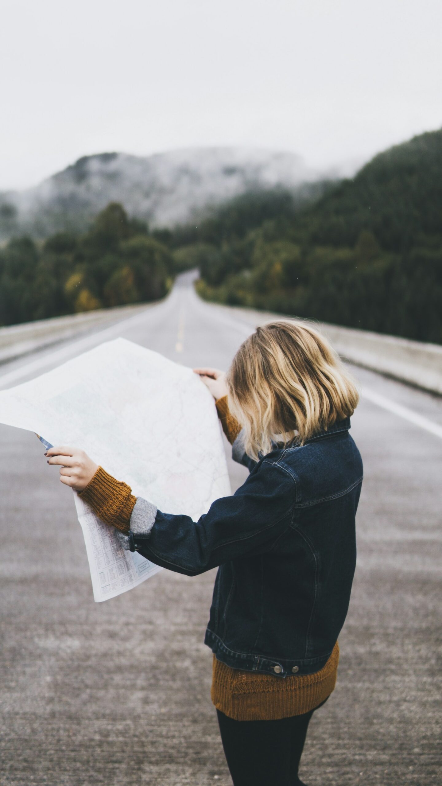 A traveler reading a large paper map while standing on a rural road