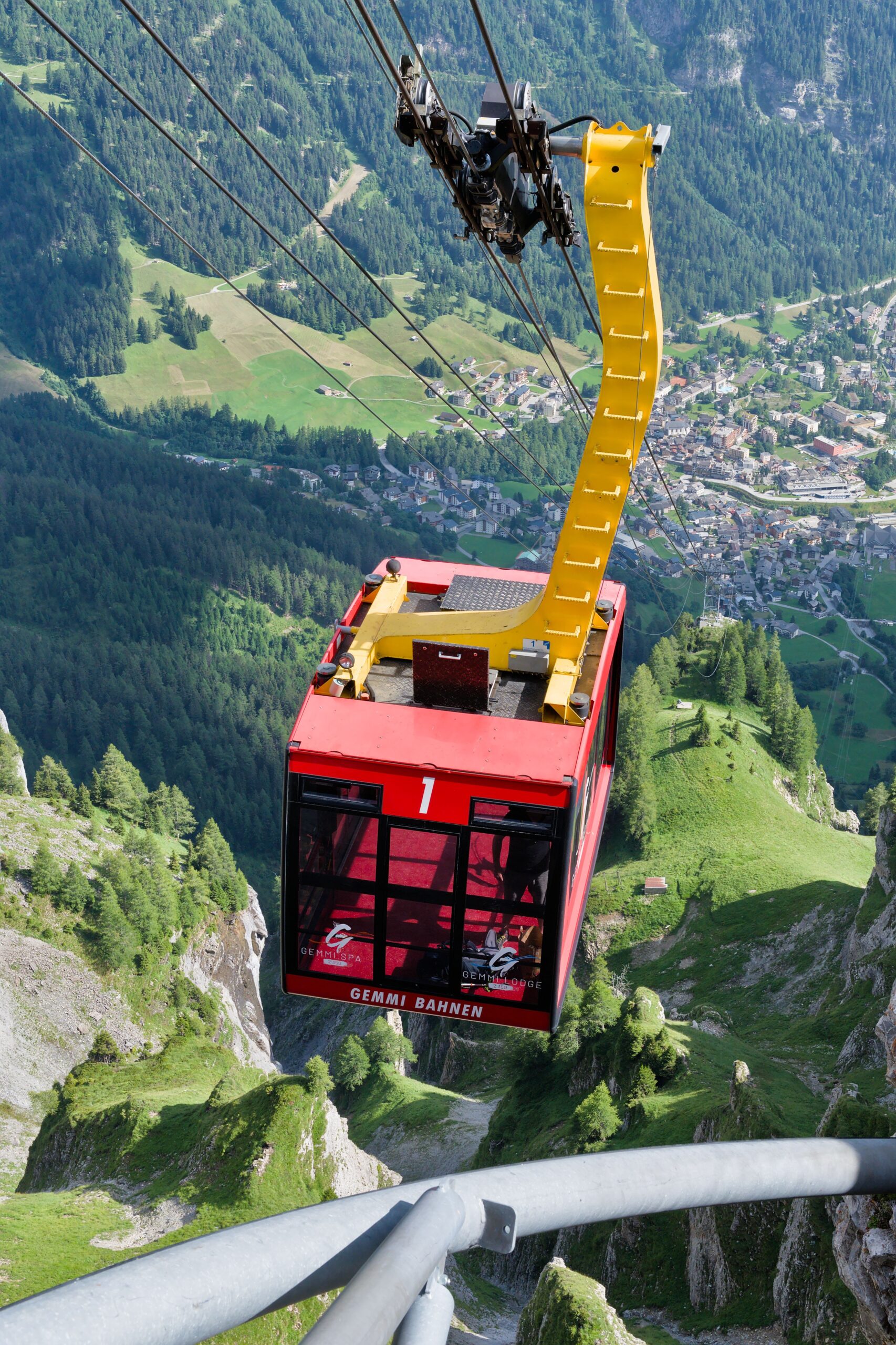 A red cable car climbs through forested peaks toward a mountaintop station