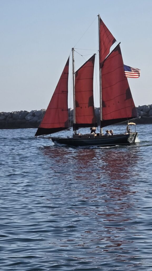 Red-sailed schooner passing the Newport Harbor jetty at Corona del Mar