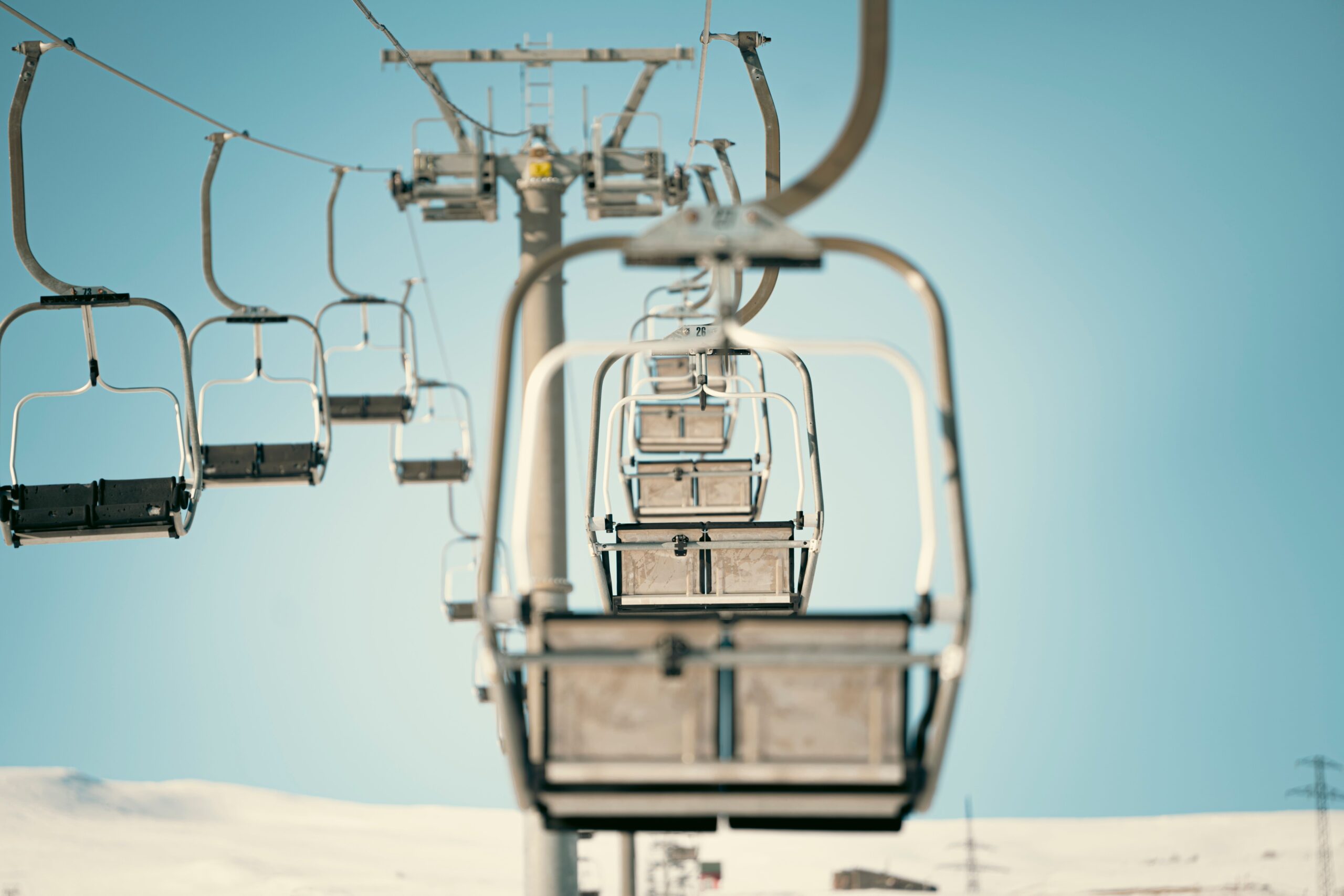 A row of empty chairlift chairs against a clear blue sky above a mountain forest