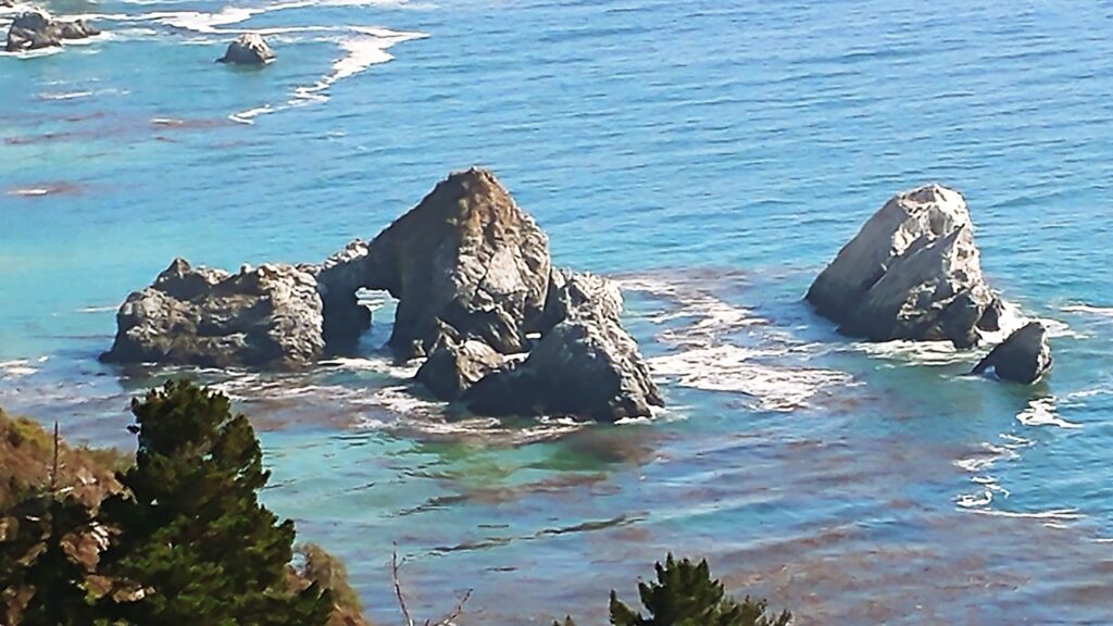 Sea stacks and a rock arch rising from blue water along the Big Sur coast