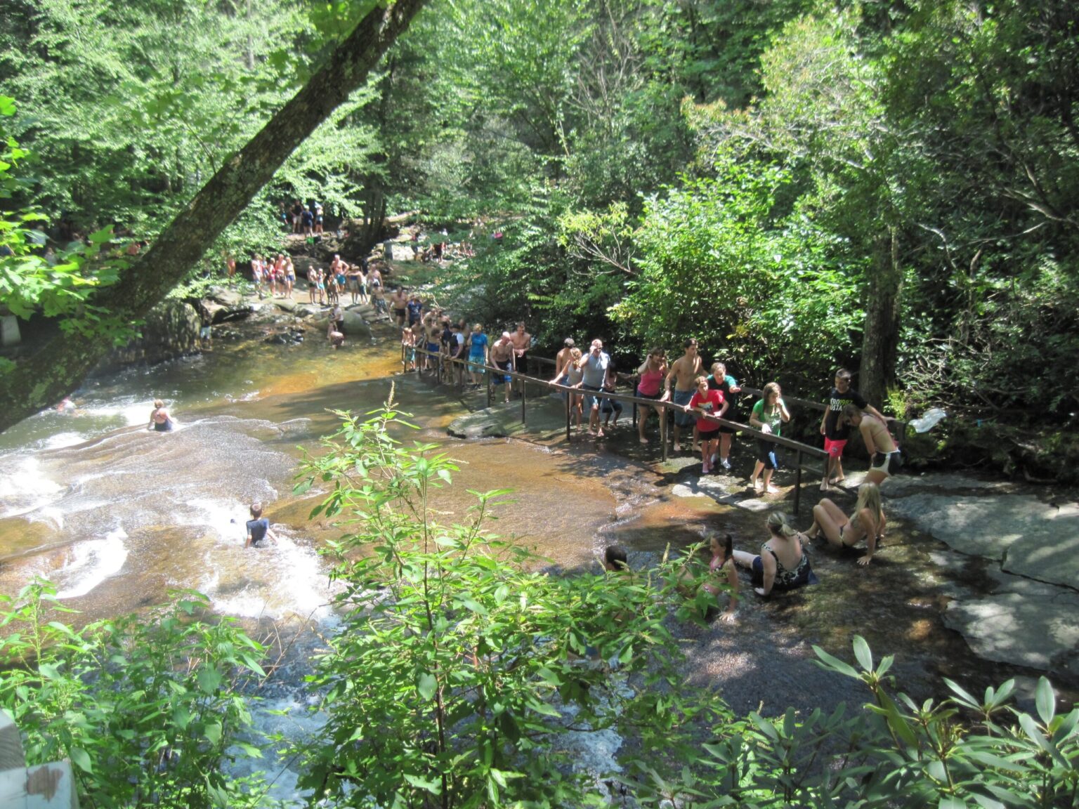A line of people crossing the rock to the top of Sliding Rock on a weekday afternoon, seen from the trail above