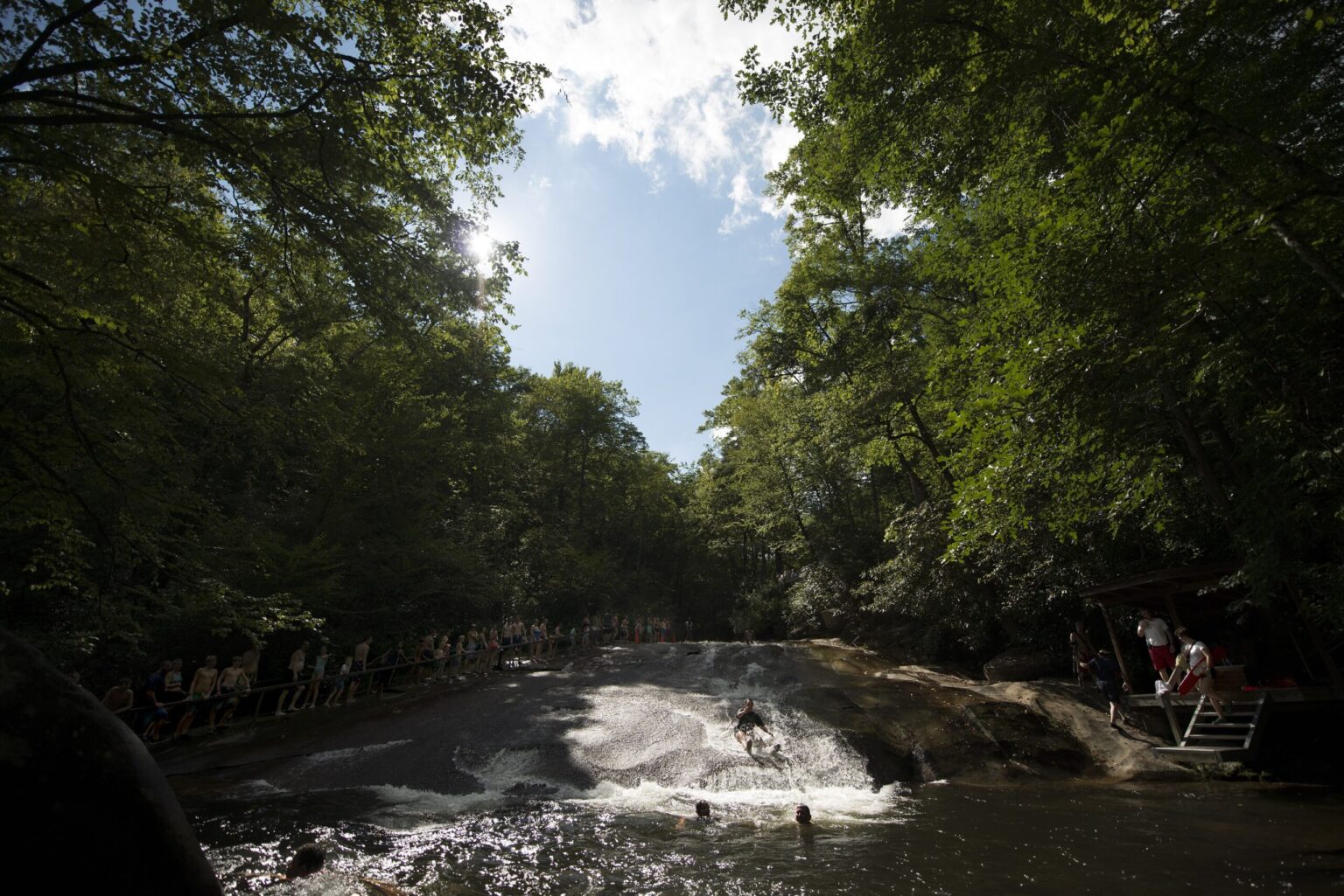 The full length of Sliding Rock seen from the plunge pool, with sliders on the rock and trees overhead