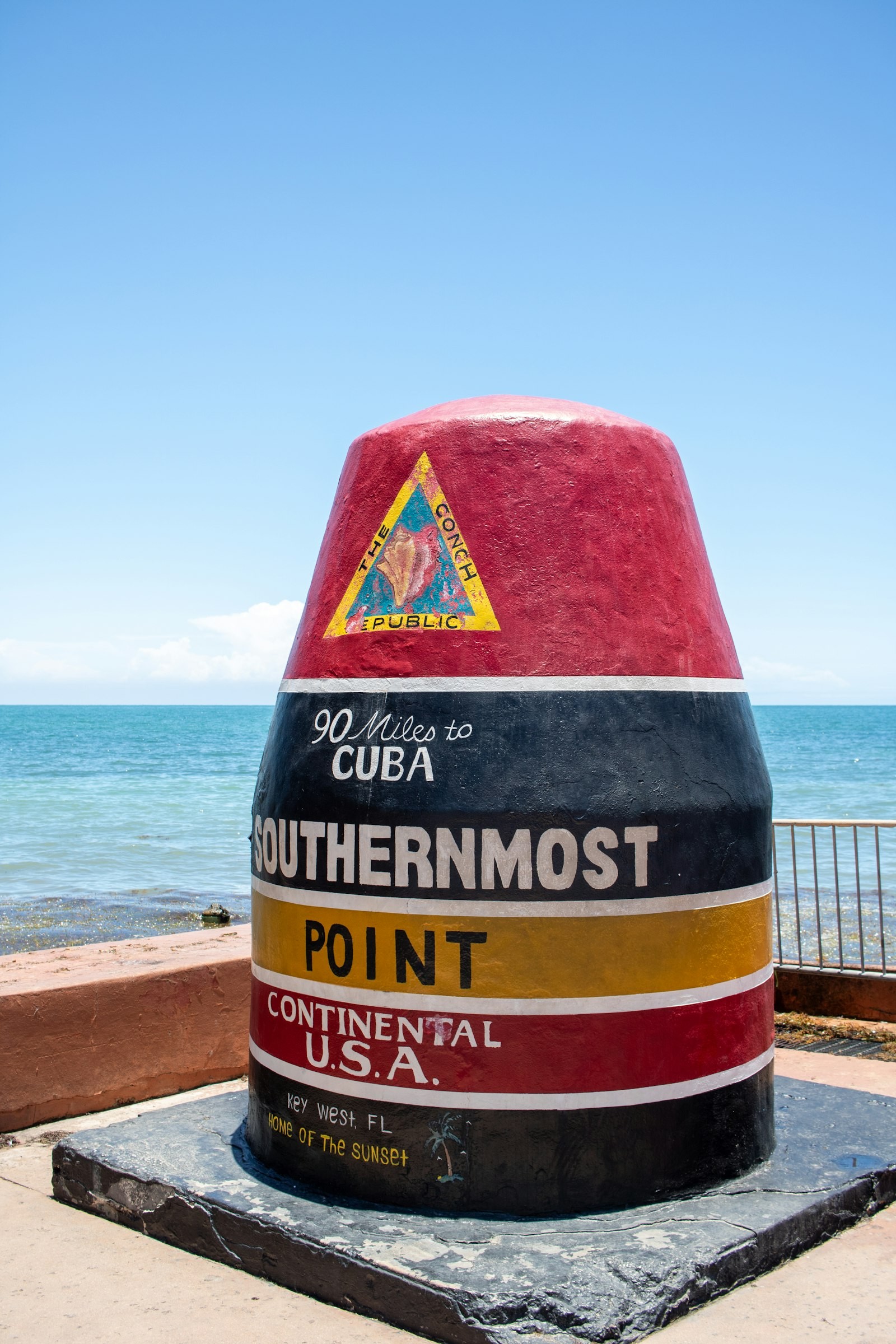 The red, black and yellow Southernmost Point buoy monument in Key West, marked 90 Miles to Cuba, with the Atlantic Ocean behind it