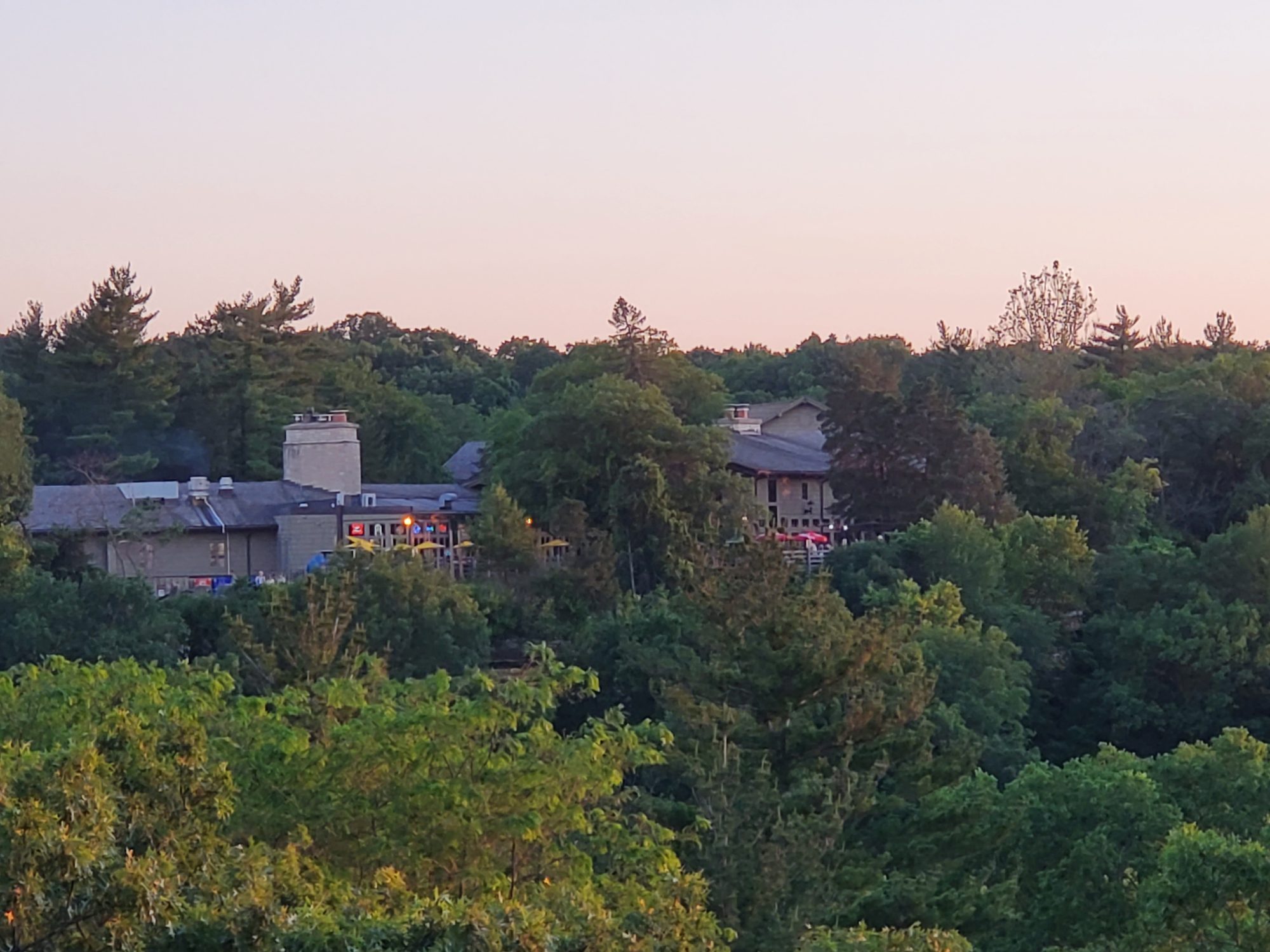 Starved Rock Lodge rooftops and stone chimney above the treeline at dusk, patio umbrellas lit below