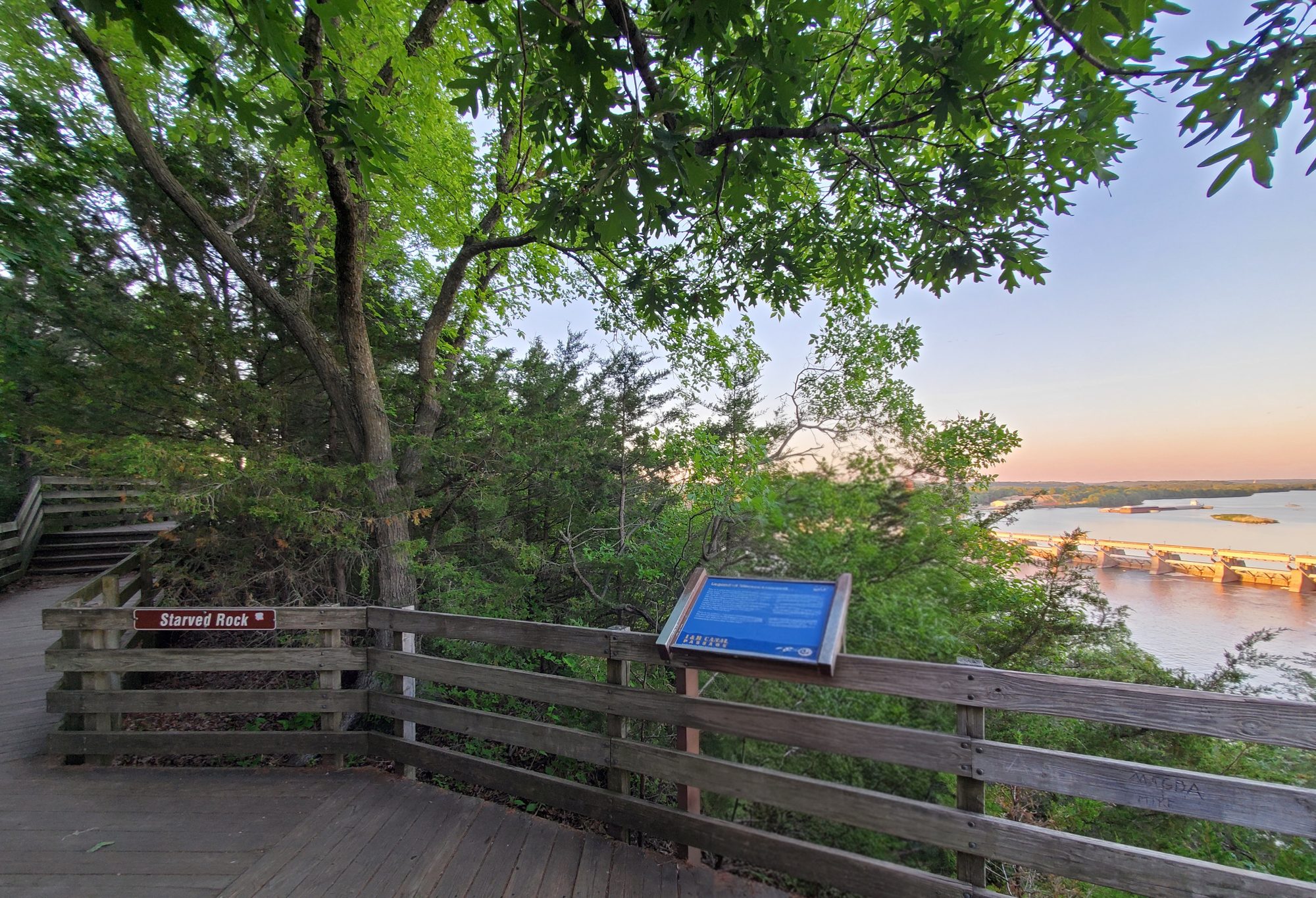 Starved Rock summit boardwalk with the Starved Rock sign, interpretive panel and the Illinois River lock and dam behind