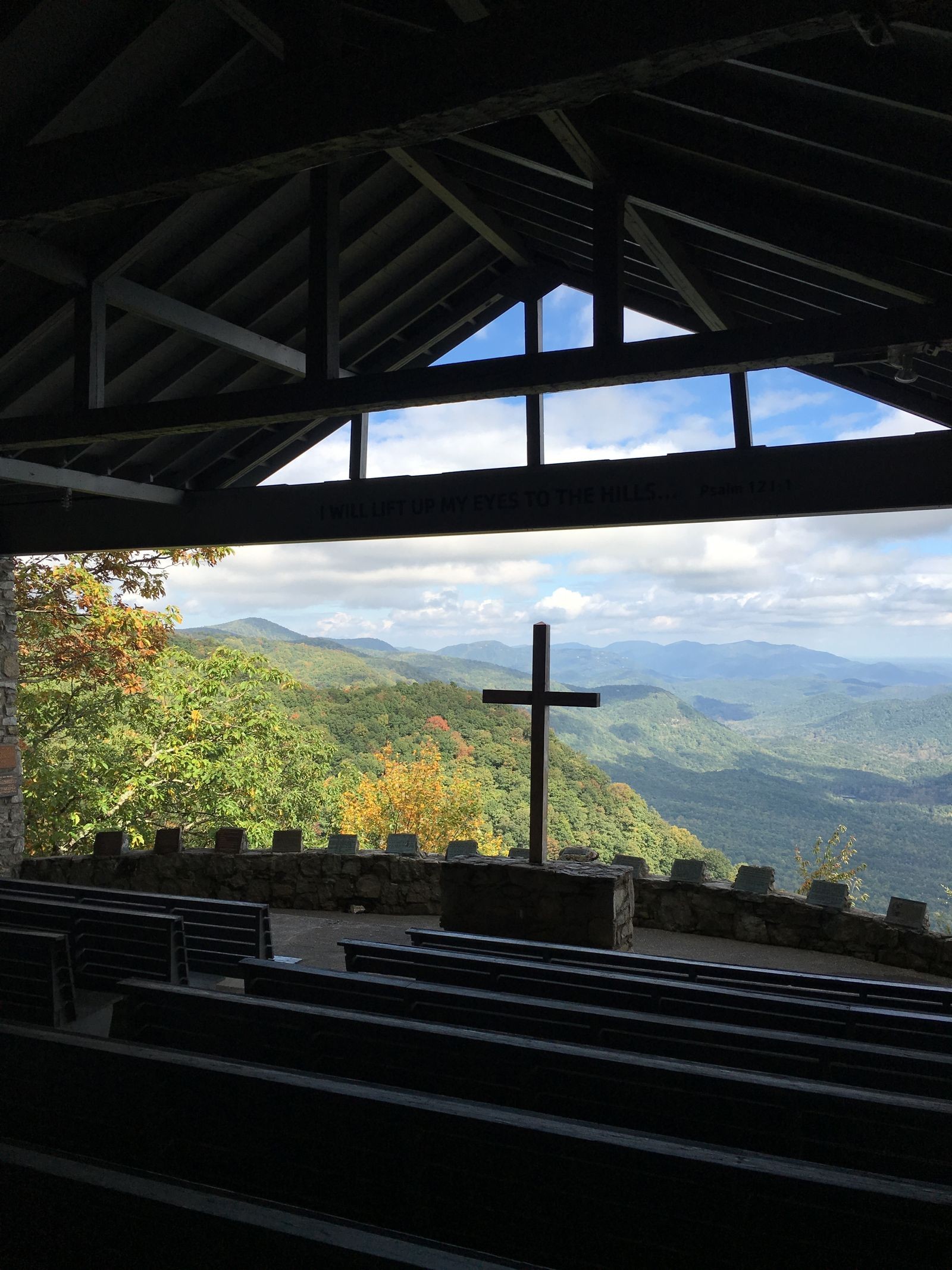 Open-air stone chapel with a wooden cross overlooking the Blue Ridge Mountains, rows of benches facing the view