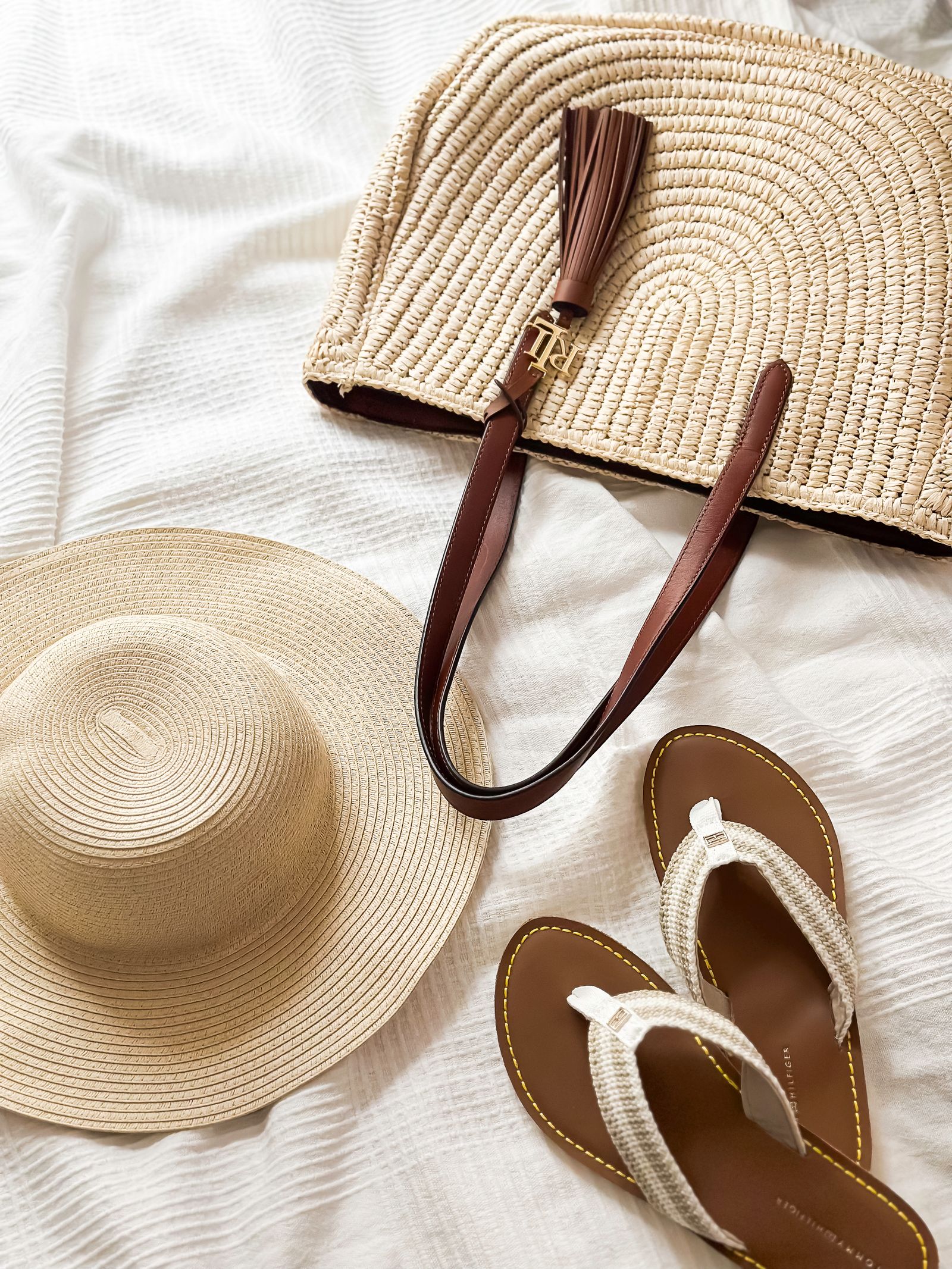 A straw hat, flip flops, and a woven bag laid out for a beach vacation packing list