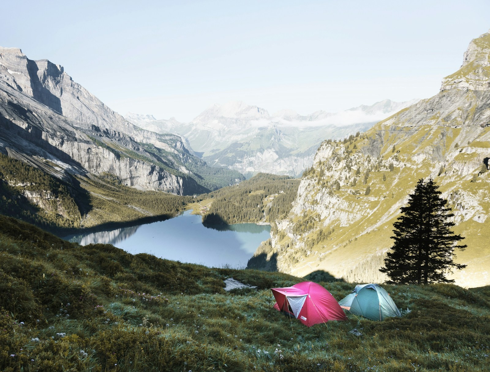 Red and grey tents pitched on a grassy mountain slope.