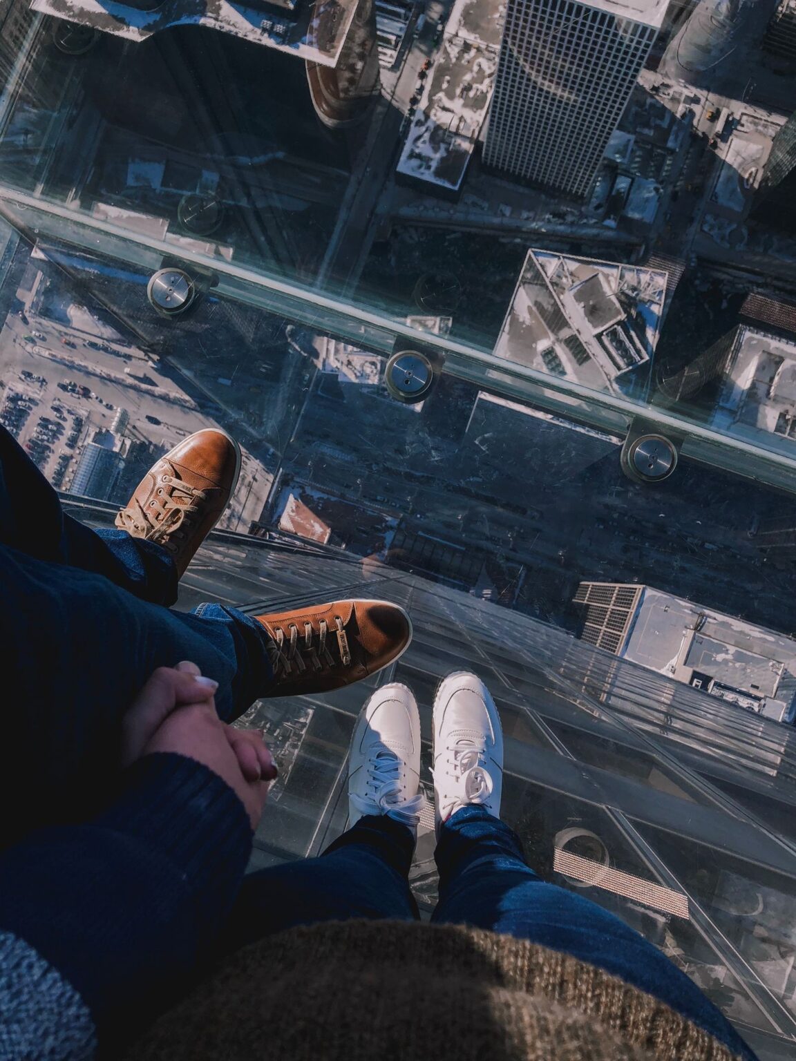 Looking straight down through the glass floor of The Ledge at Skydeck Chicago, two visitors' feet on the glass with the city street grid far below