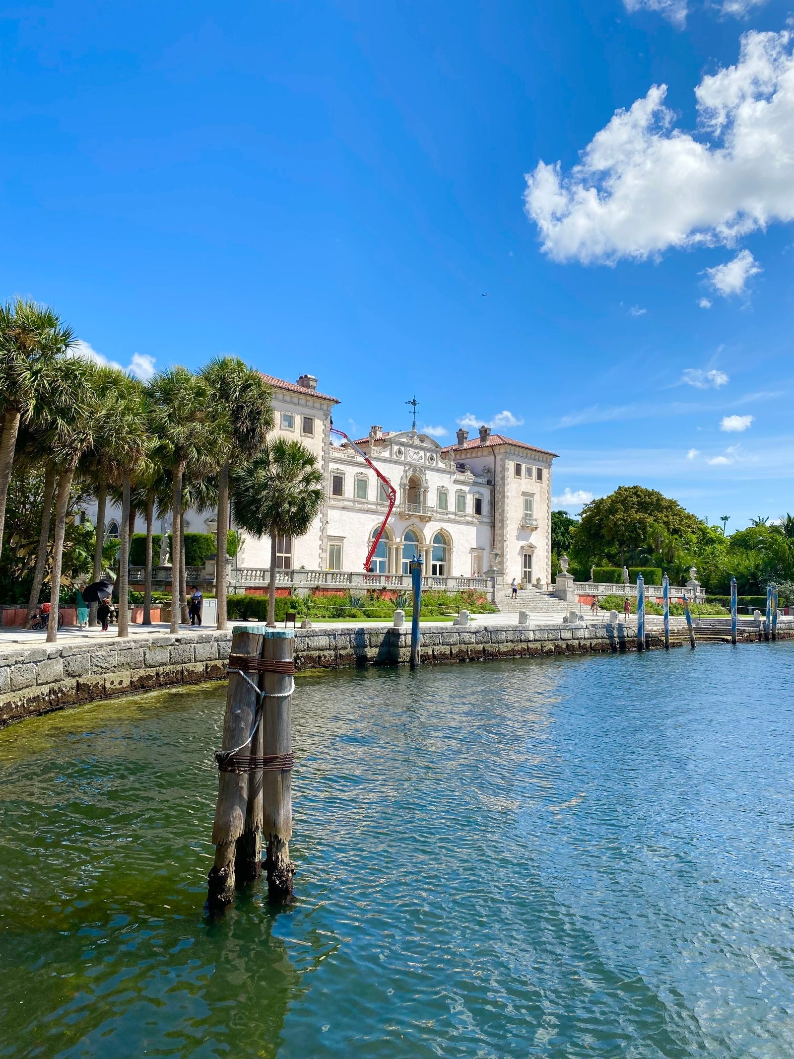 The Vizcaya villa seen from Biscayne Bay, with palm trees along the seawall and mooring piles in the green water in the foreground