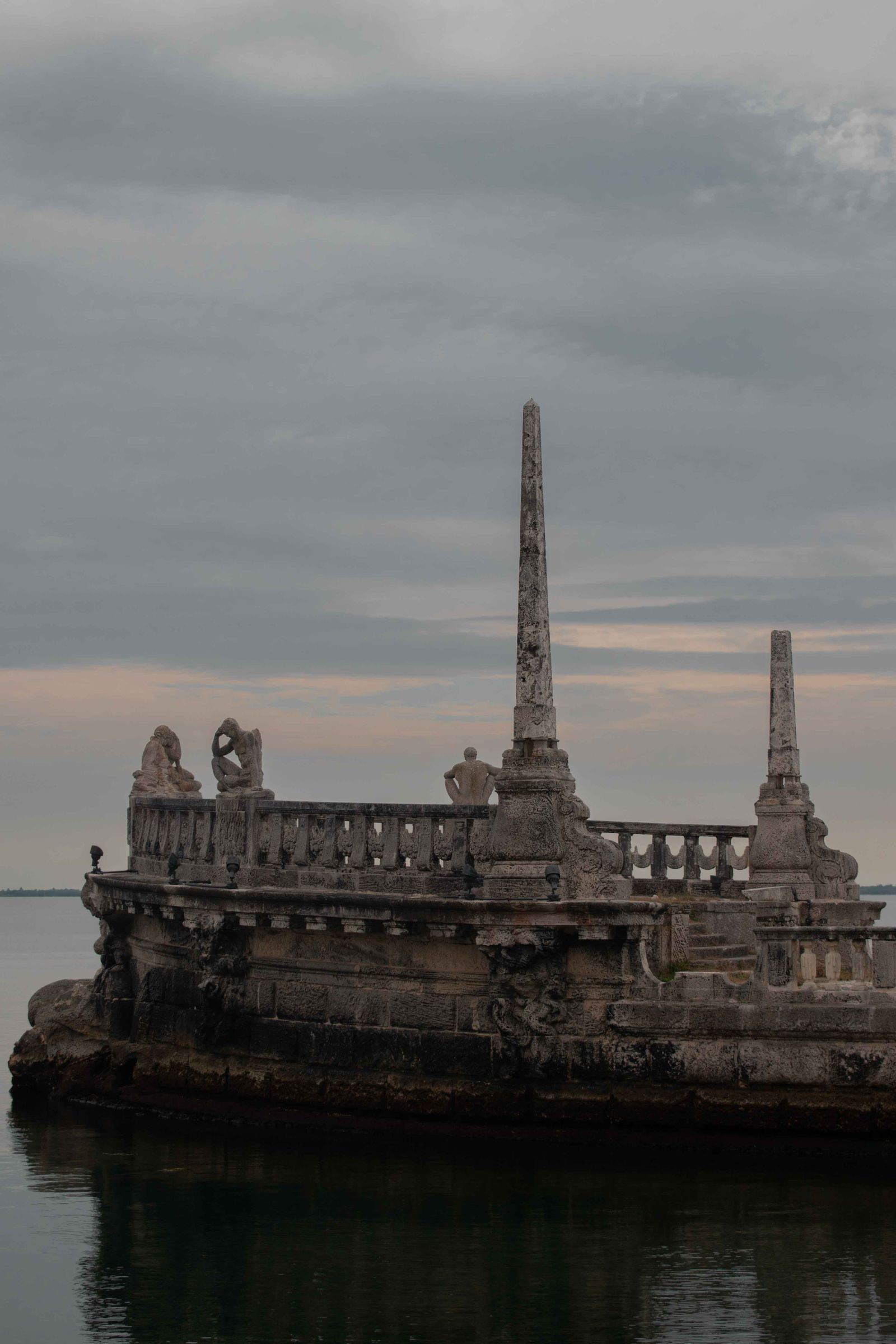 The carved stone barge breakwater at Vizcaya silhouetted on Biscayne Bay at dusk, with obelisks and reclining stone figures along its deck