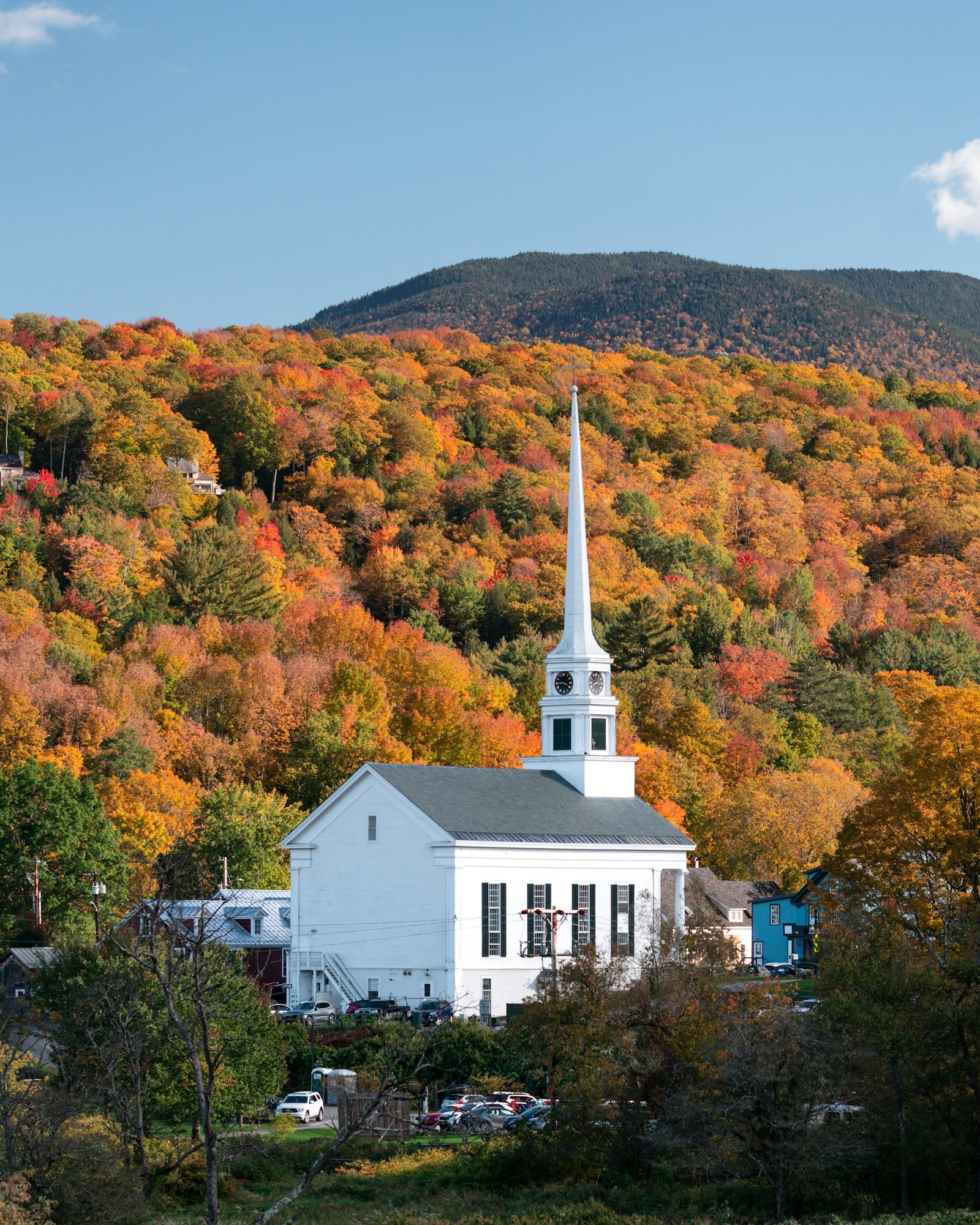 A white building with a steeple surrounded by trees and a hillside.