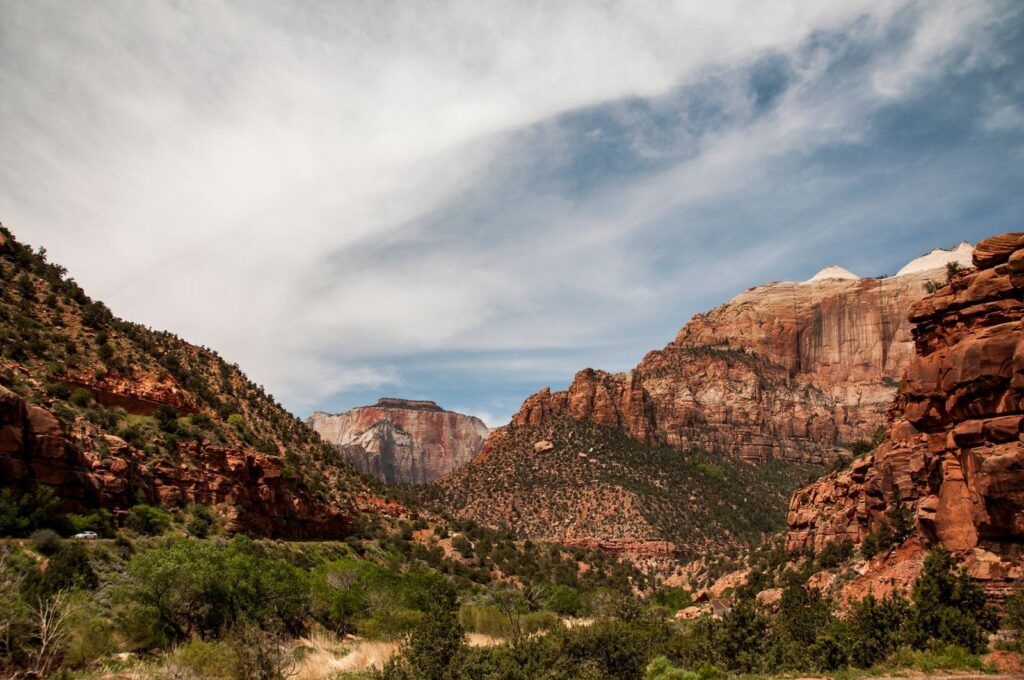 Zion Canyon's red and white sandstone cliffs rising above a green valley, with the scenic drive road visible below