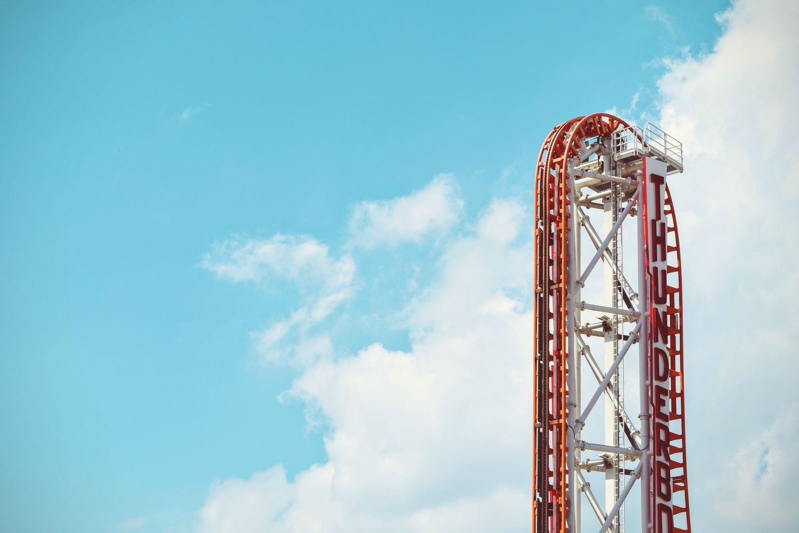 A roller coaster track rising into a bright blue sky with scattered clouds