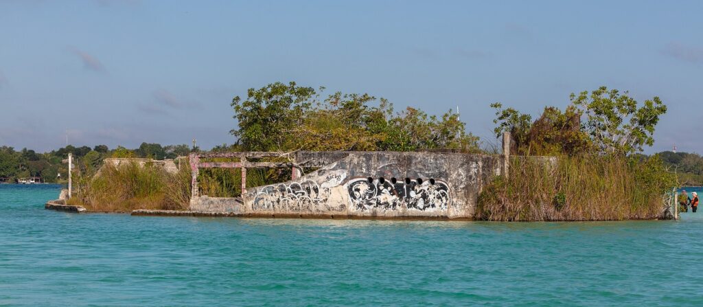 A weathered, graffiti-covered ship hull in turquoise water at the Canal de los Piratas on Bacalar lagoon