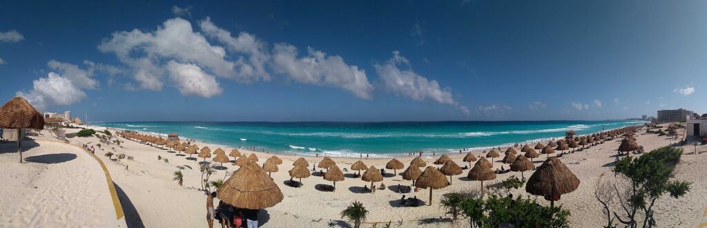 Wide beach with thatched palapas and turquoise water at Delfines Beach in Cancun
